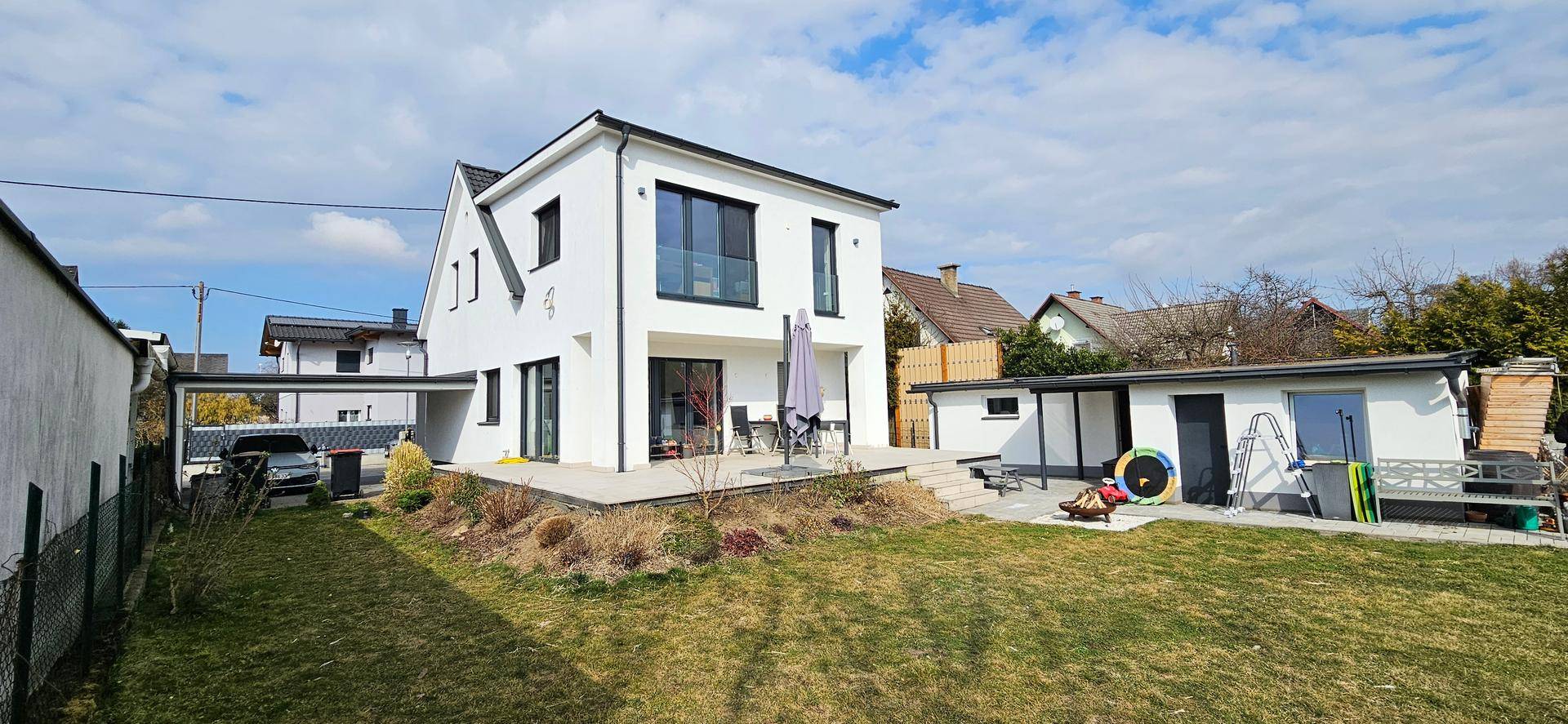 Großer Garten mit Rasenfläche, Terrasse und Blick auf das moderne Einfamilienhaus.