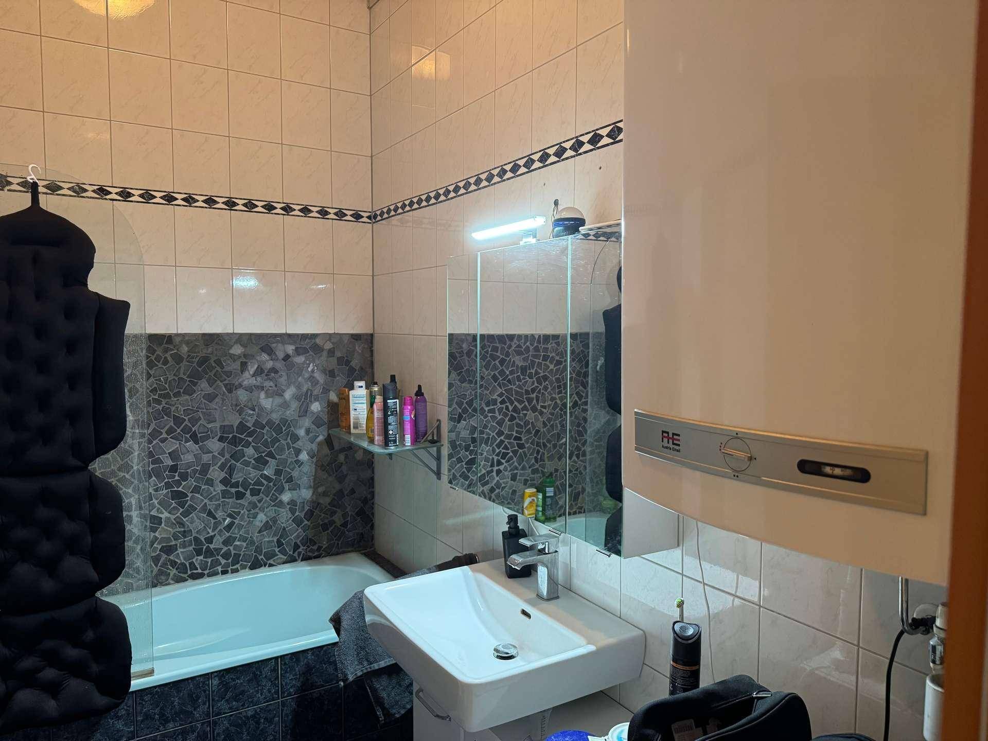 Badezimmer mit Badewanne, Duschwand, Waschbecken und Fliesen in klassischem Design.