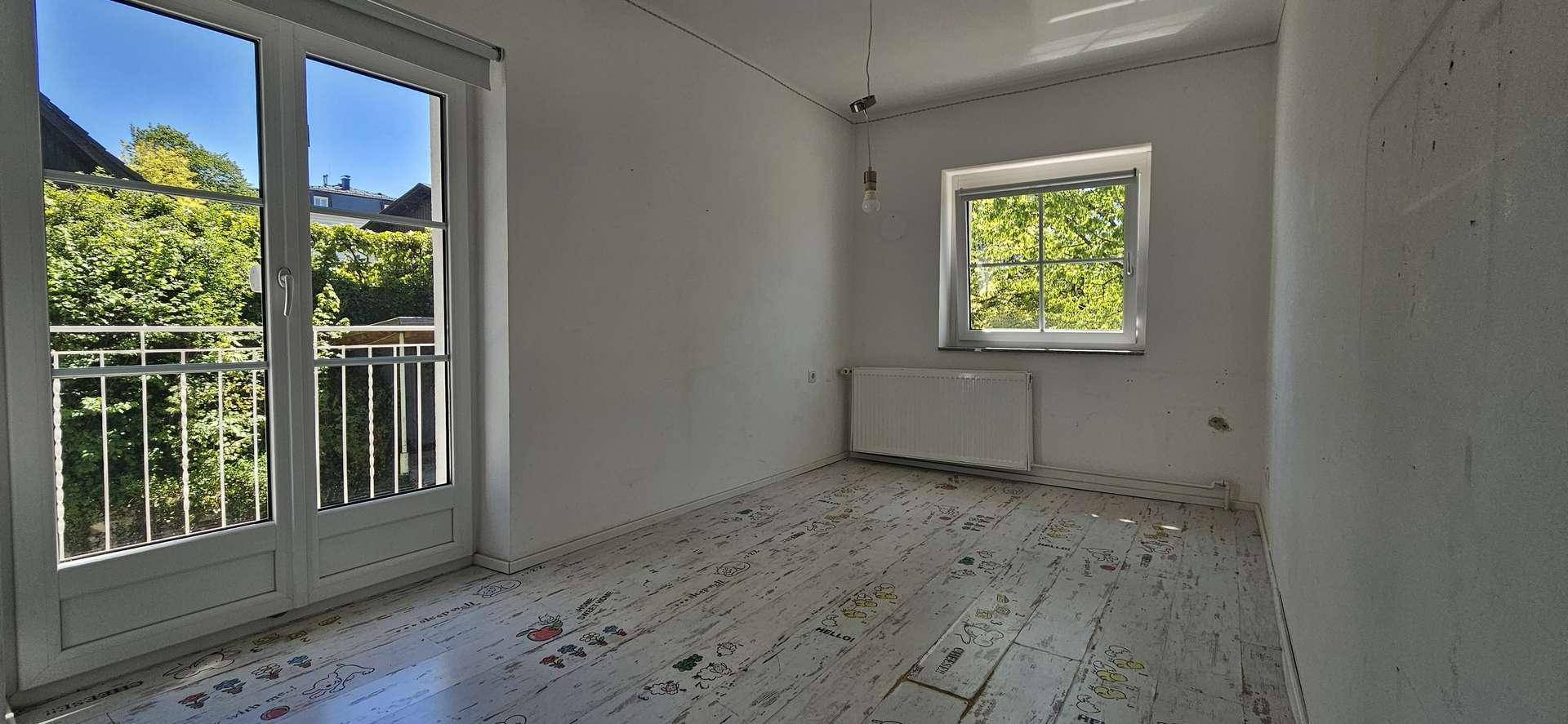 Helles Schlafzimmer mit gemustertem Boden, Fenster und Balkonzugang, bietet einen Blick ins Grüne.