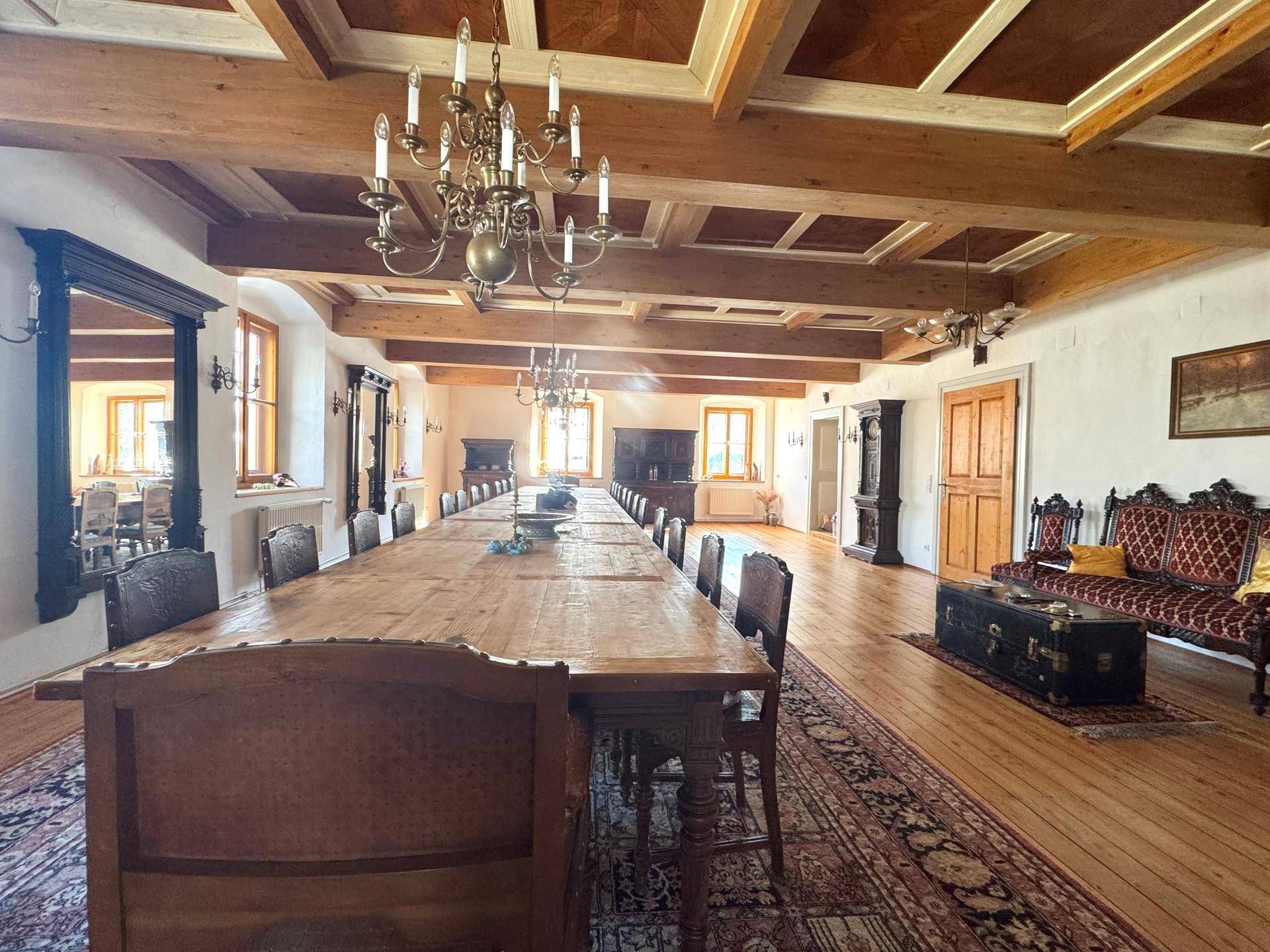 Sehr großer Speisesaal mit Holzbalkendecke, langer Holztafel und Kronleuchtern.