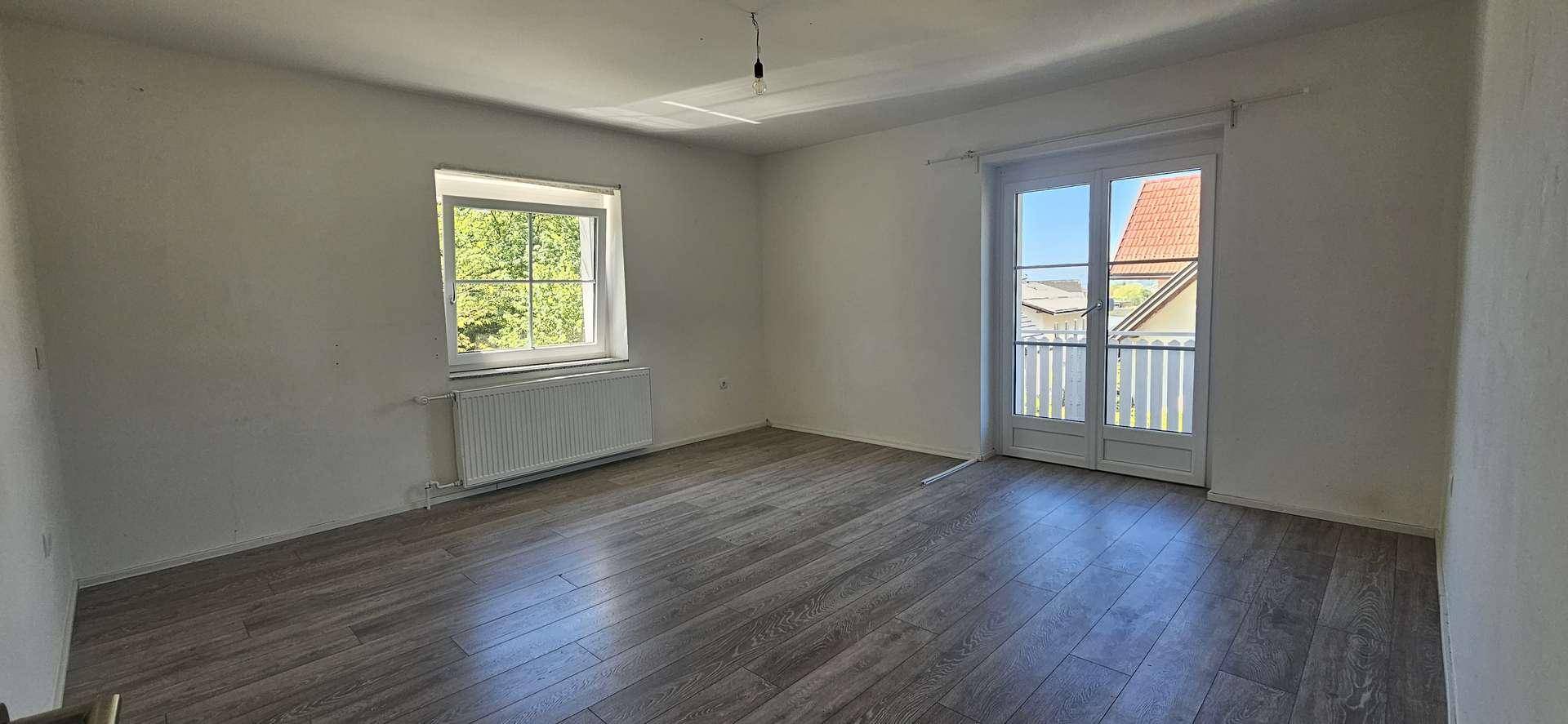 Geräumiges Schlafzimmer mit Laminatboden, Heizkörper und Zugang zu einem Balkon mit Blick nach draußen.