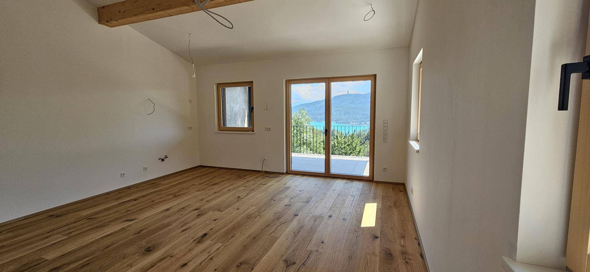 Heller Wohnraum mit Echtholzboden, hohen Decken und direktem Zugang zu einem Balkon mit Seeblick.