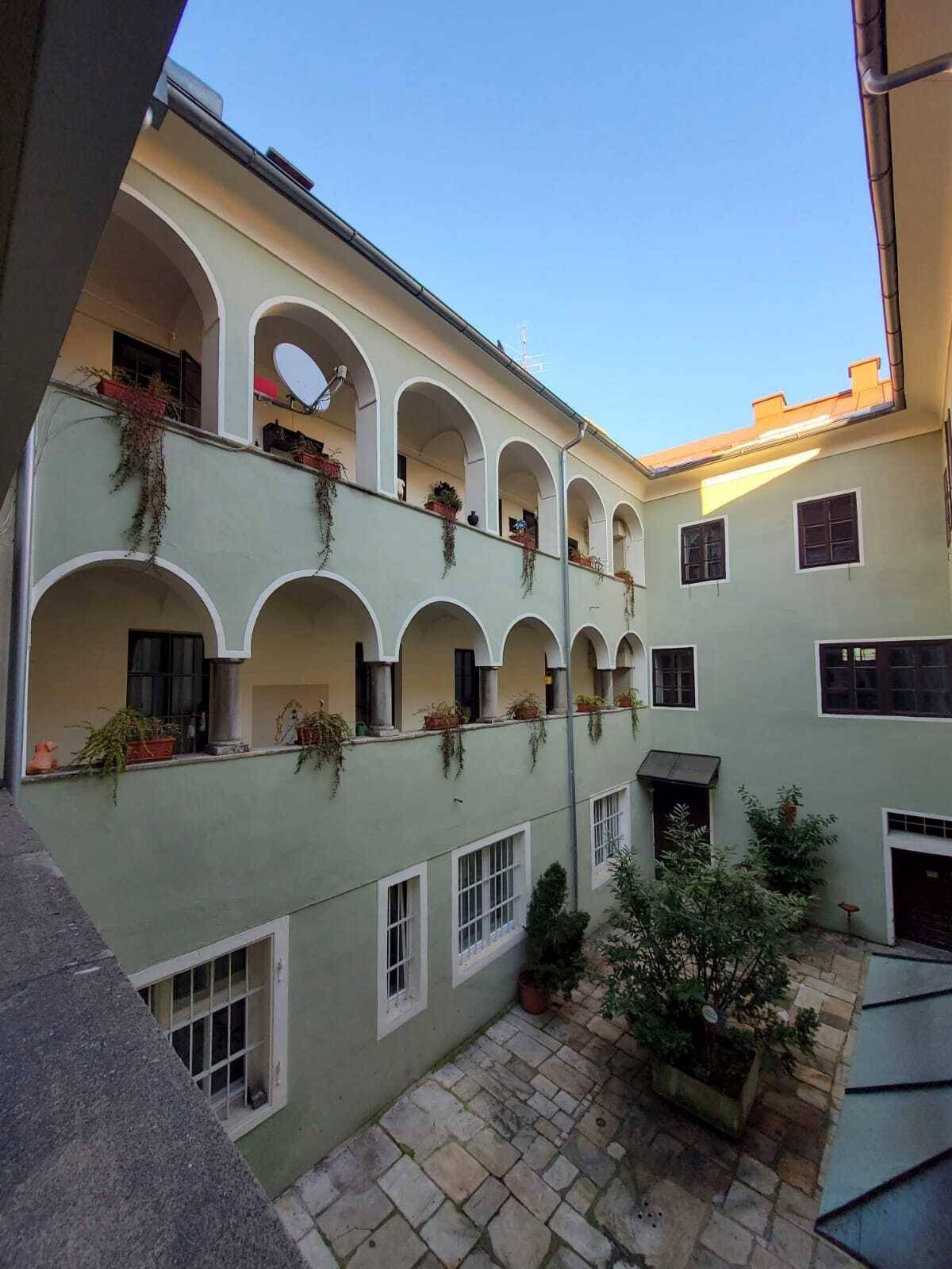 Blick in den Innenhof eines Altbaus mit Arkadengängen und begrünten Balkonen.