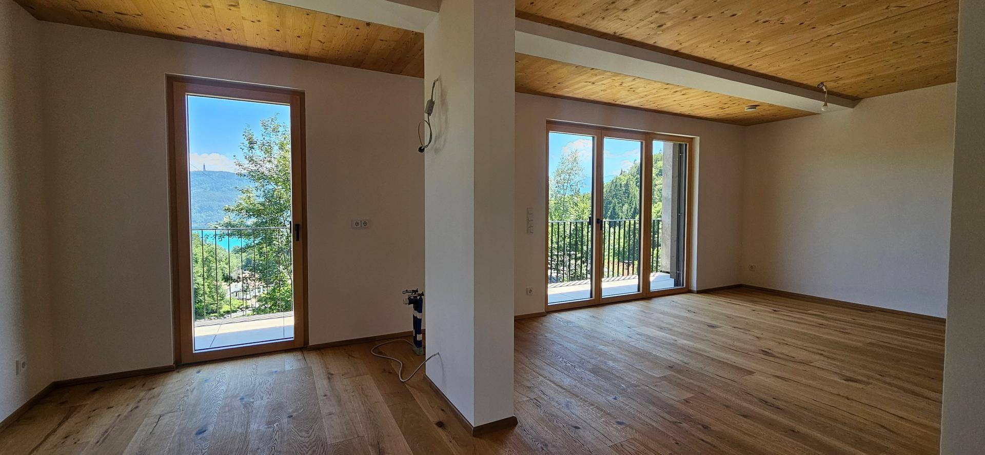 Heller Wohnraum mit Holzboden, Holzdecke und Zugang zu einem Balkon mit Seeblick.