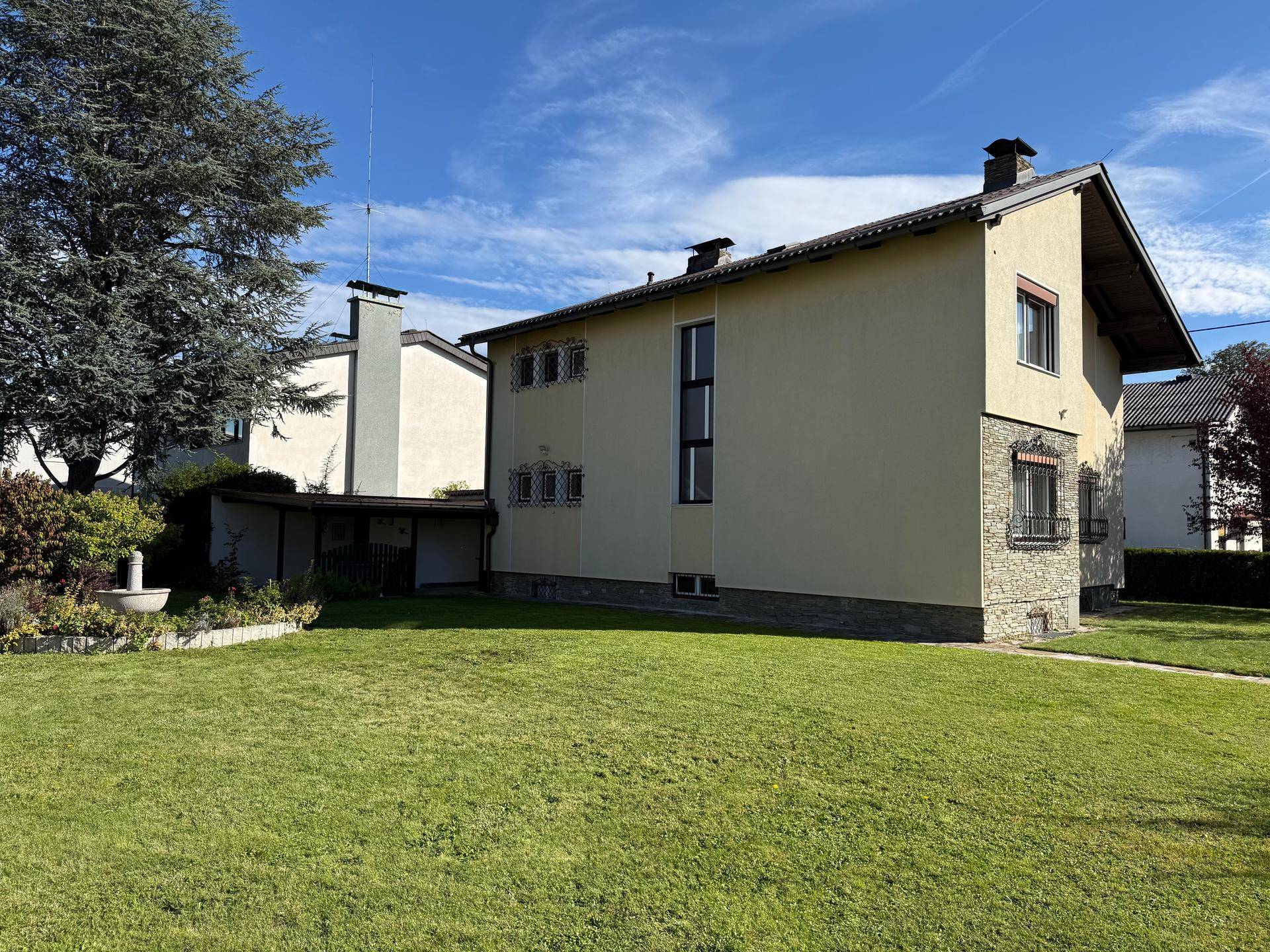 Seitenansicht des Hauses mit weitläufigem Rasen und einem großen Baum im Garten.