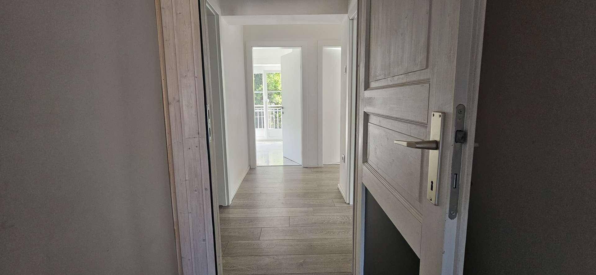 Heller Flur mit Laminatboden und weißen Wänden, der zu weiteren Zimmern mit viel Tageslicht führt.
