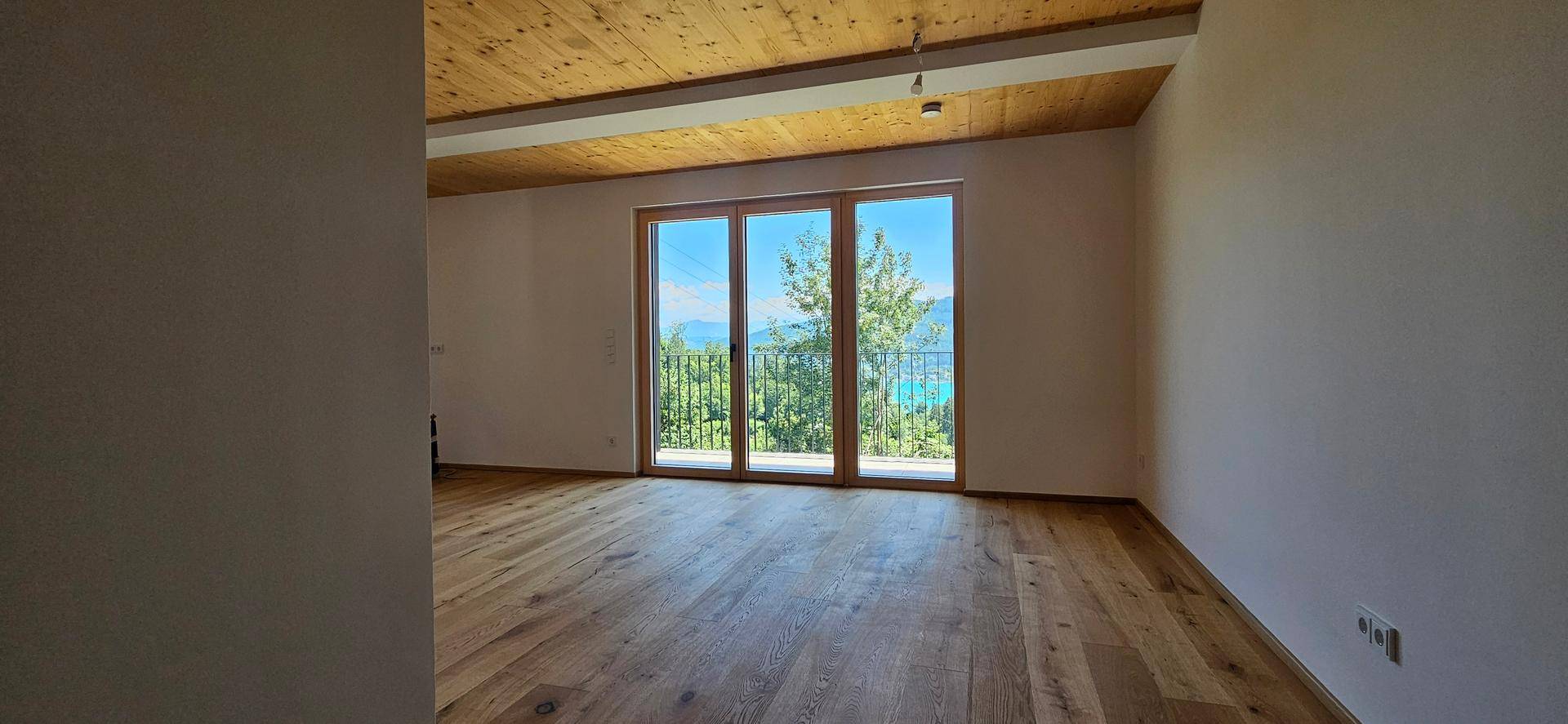 Geräumiger Wohnraum mit Holzboden und großen Fenstern, die einen weiten Blick auf den See bieten.