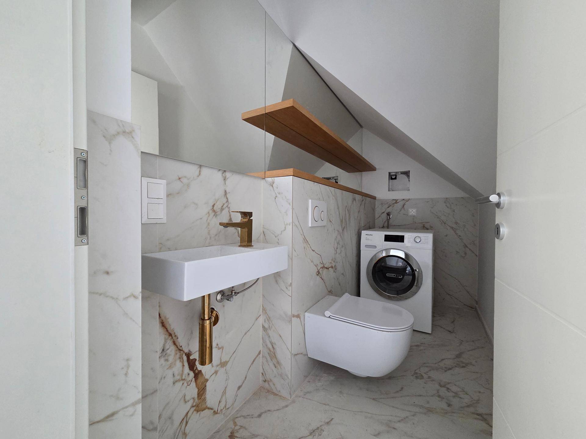 Modernes Gäste-WC im Dachgeschoss mit Marmorfliesen, Waschmaschine und goldenen Armaturen.