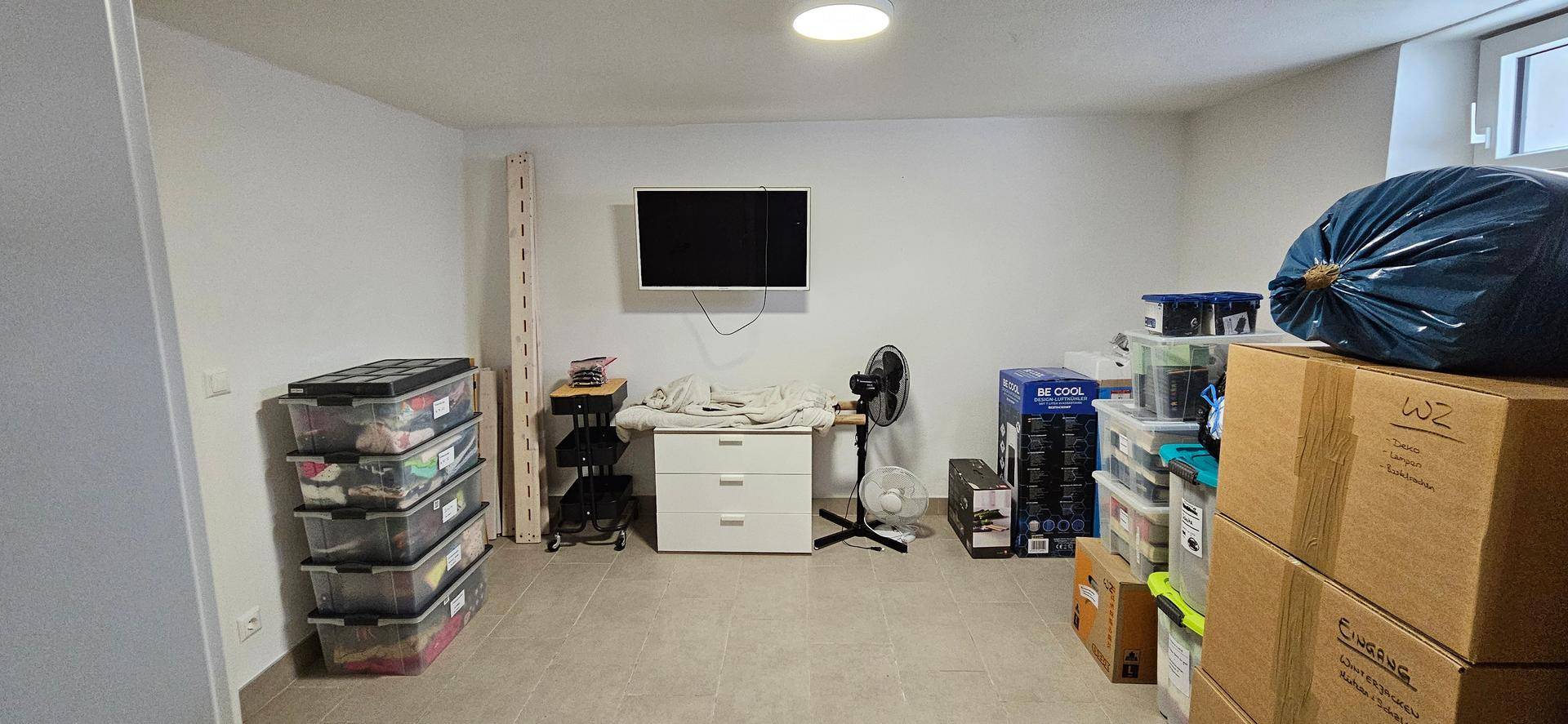 Geräumiger Kellerraum mit Fliesenboden, Fernseher und viel Stauraum.