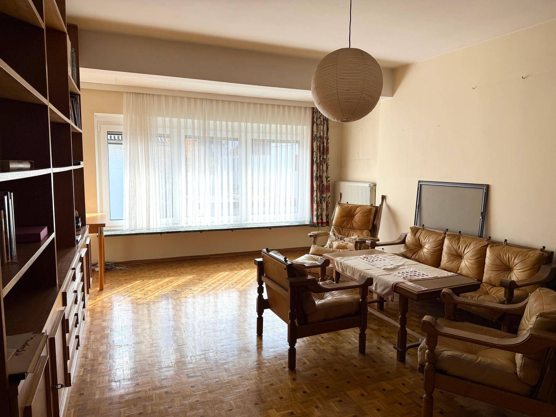 Helles Wohnzimmer mit Vintage-Möbeln, großem Fenster und klassischem Parkettboden.