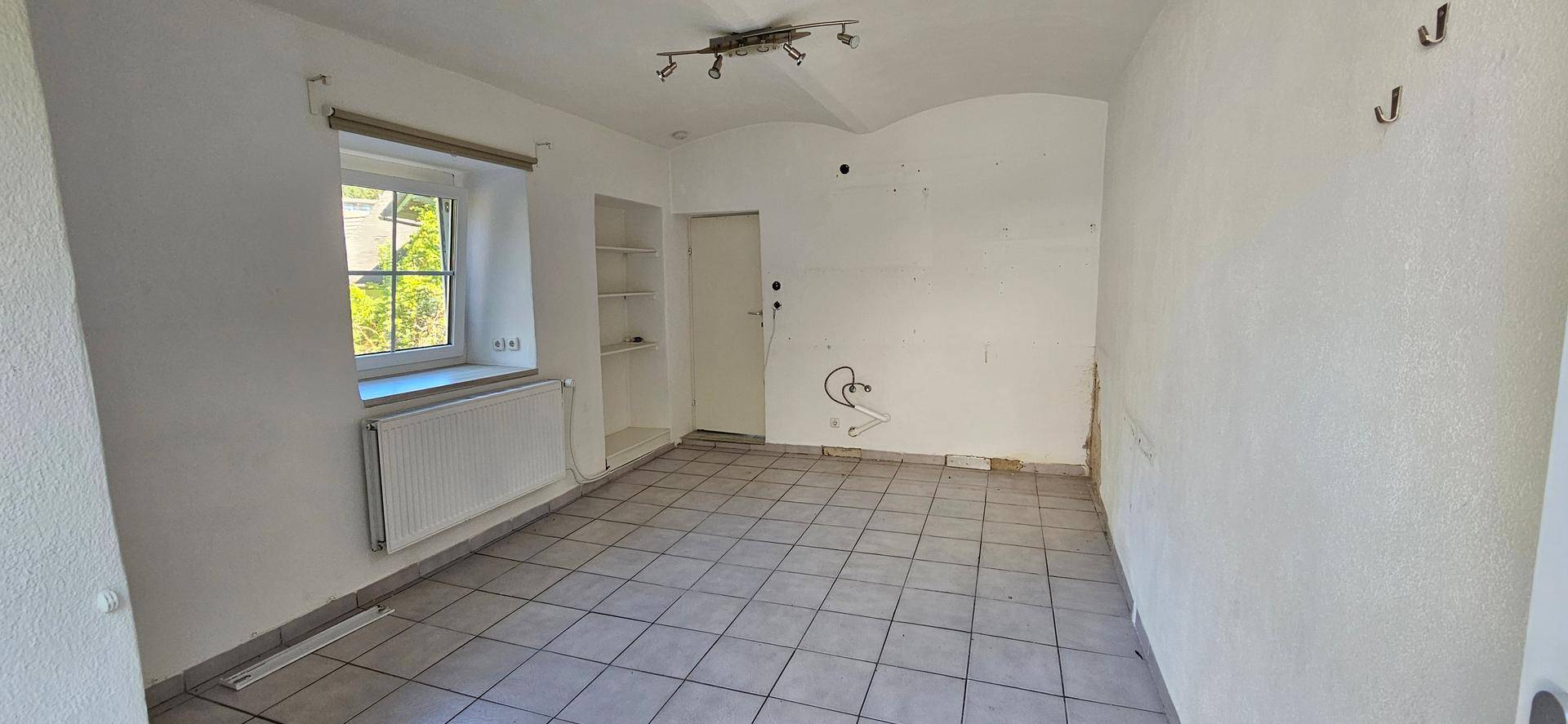 Helles Zimmer mit Fliesenboden und Fenster, bereit zur individuellen Gestaltung.