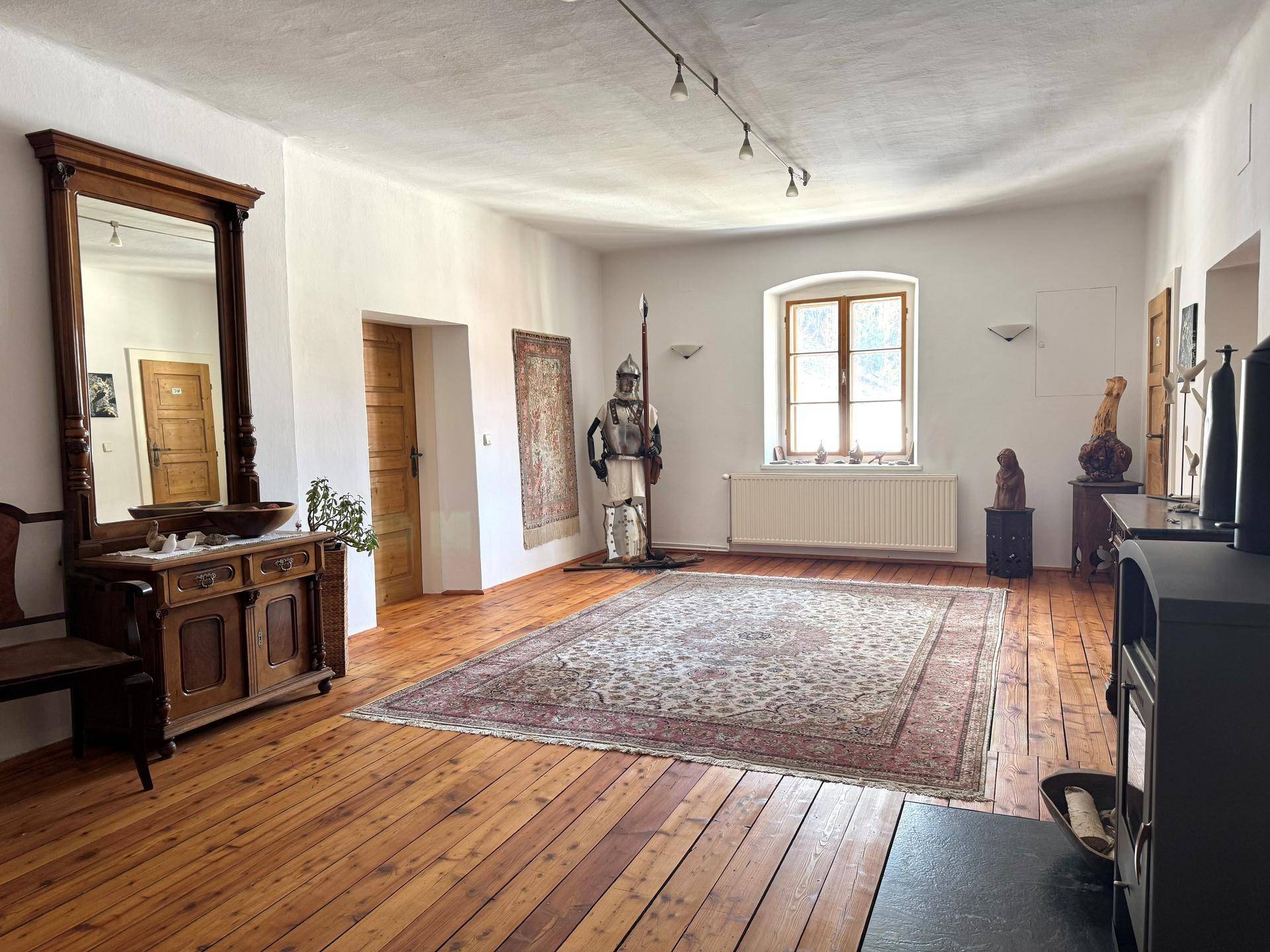 Geräumiger Raum mit Holzdielenboden, Kaminofen und historischer Dekoration.