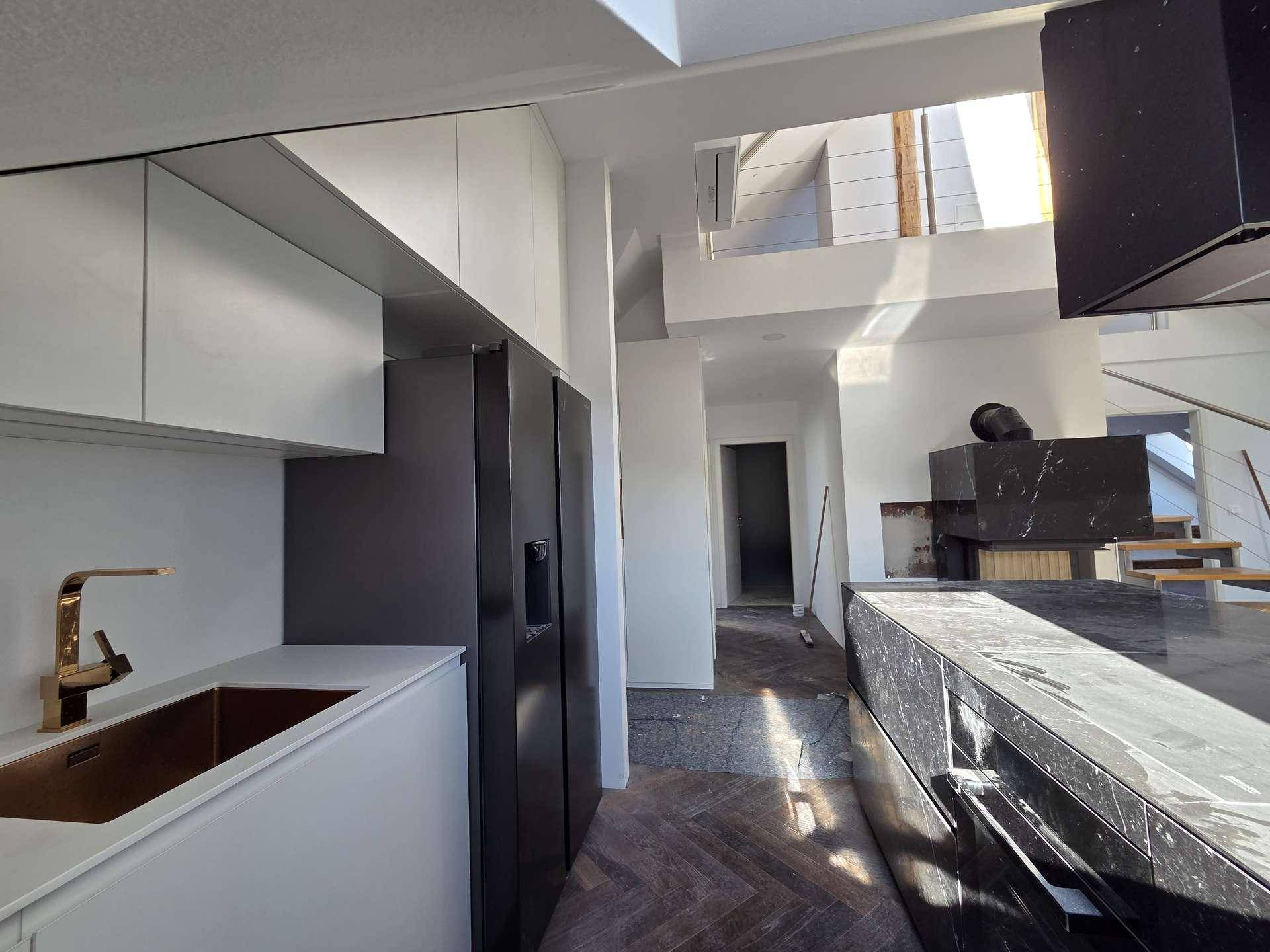Helle Küche mit weißen Schränken, schwarzem Kühlschrank und goldener Armatur neben der Marmorinsel.
