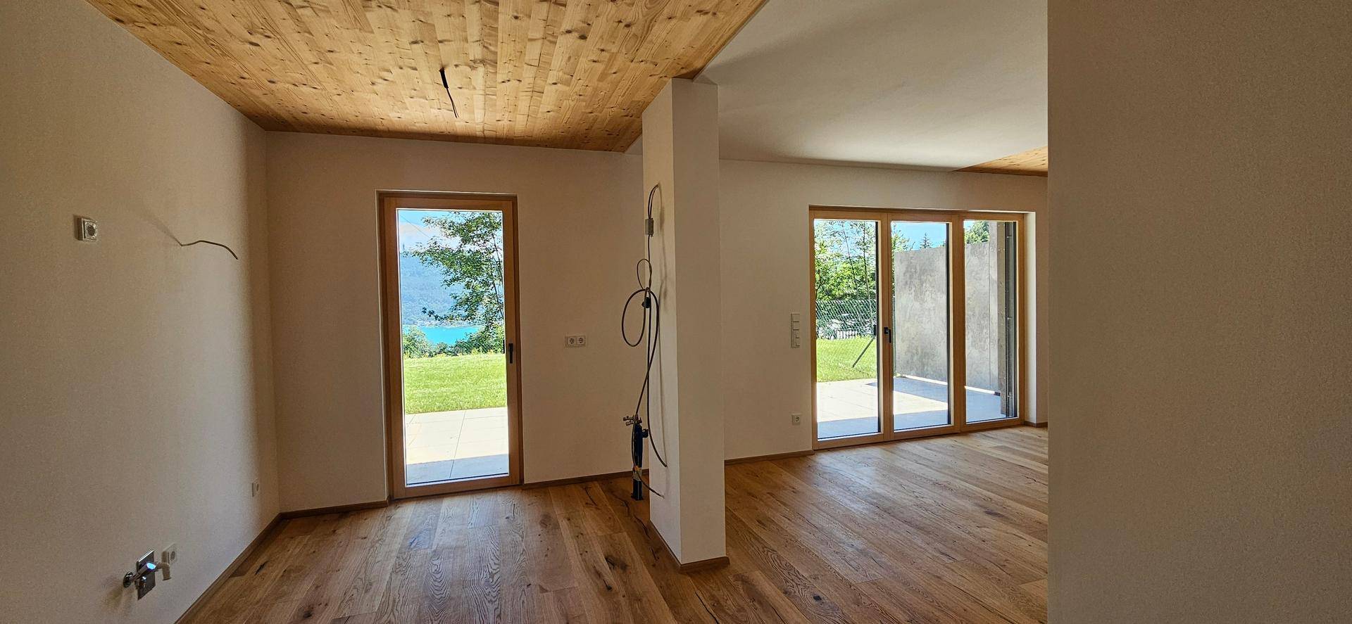 Heller, unmöblierter Wohnraum mit Holzboden, Holzdecke und großen Fenstern mit Seeblick.