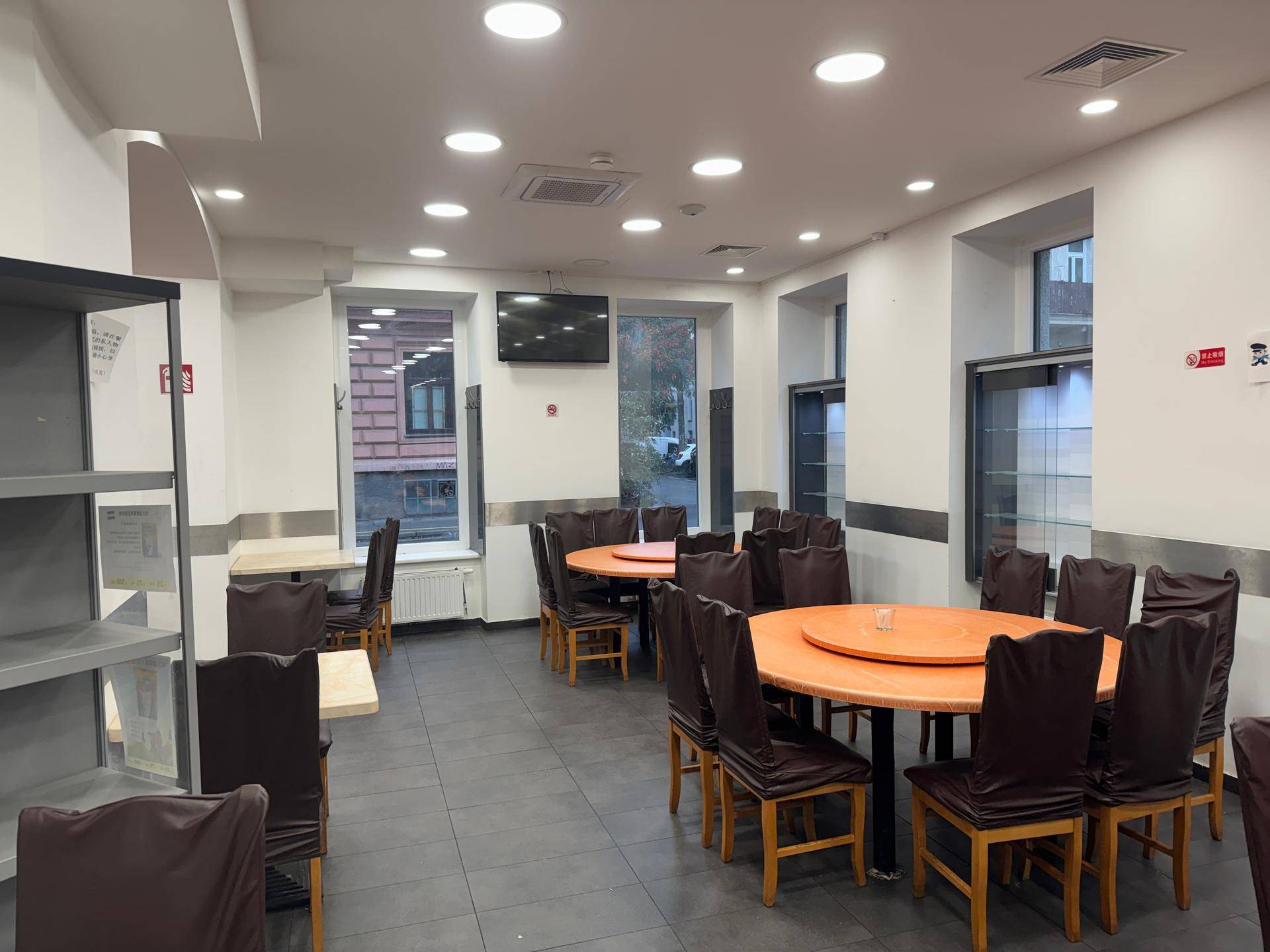 Restaurantinterieur mit runden Tischen, dunklen Stühlen und Blick auf die Straße durch die Fenster.