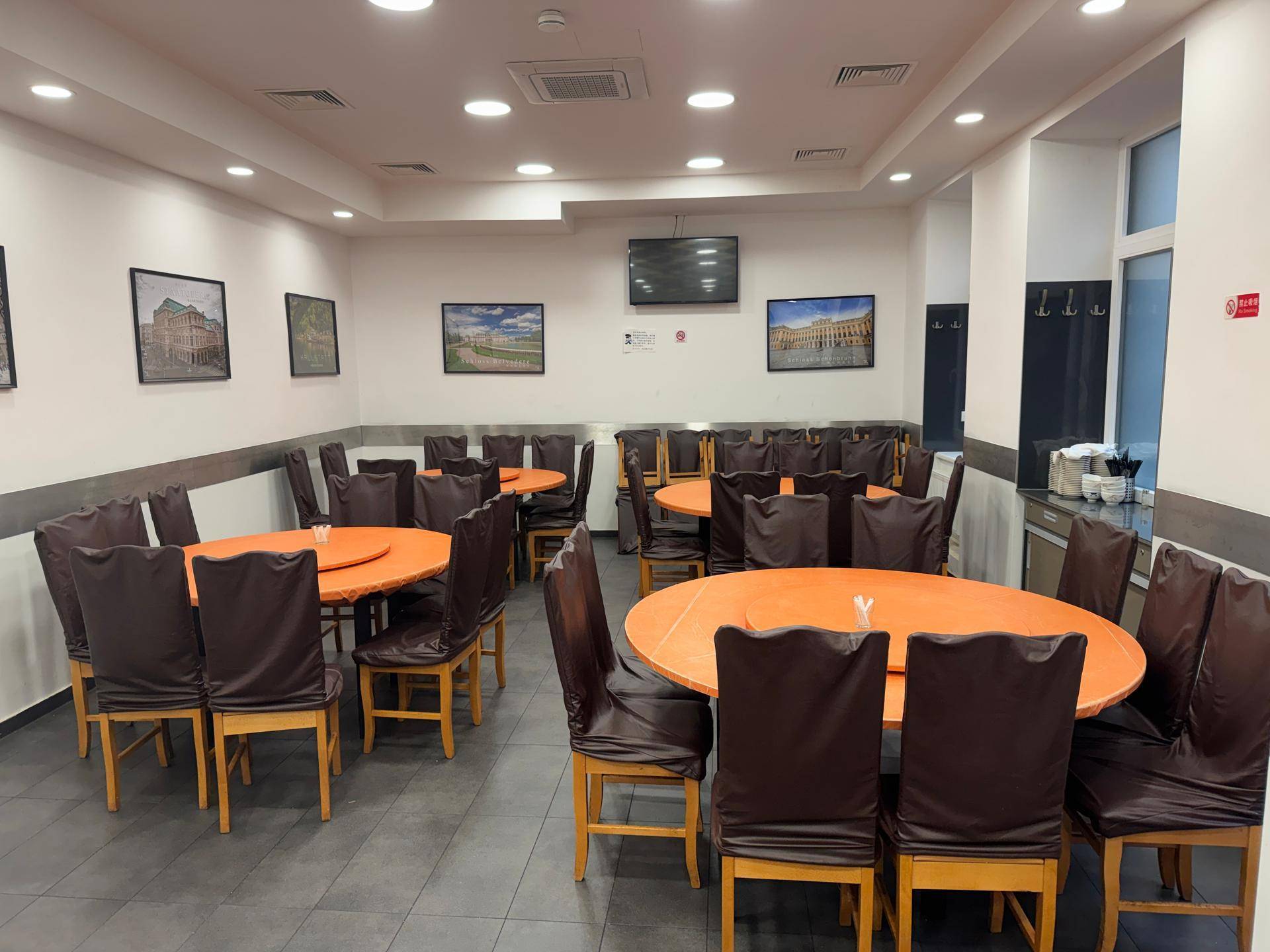 Geräumiger Restaurantbereich mit runden Tischen, dunklen Stühlen und Fliesenboden.