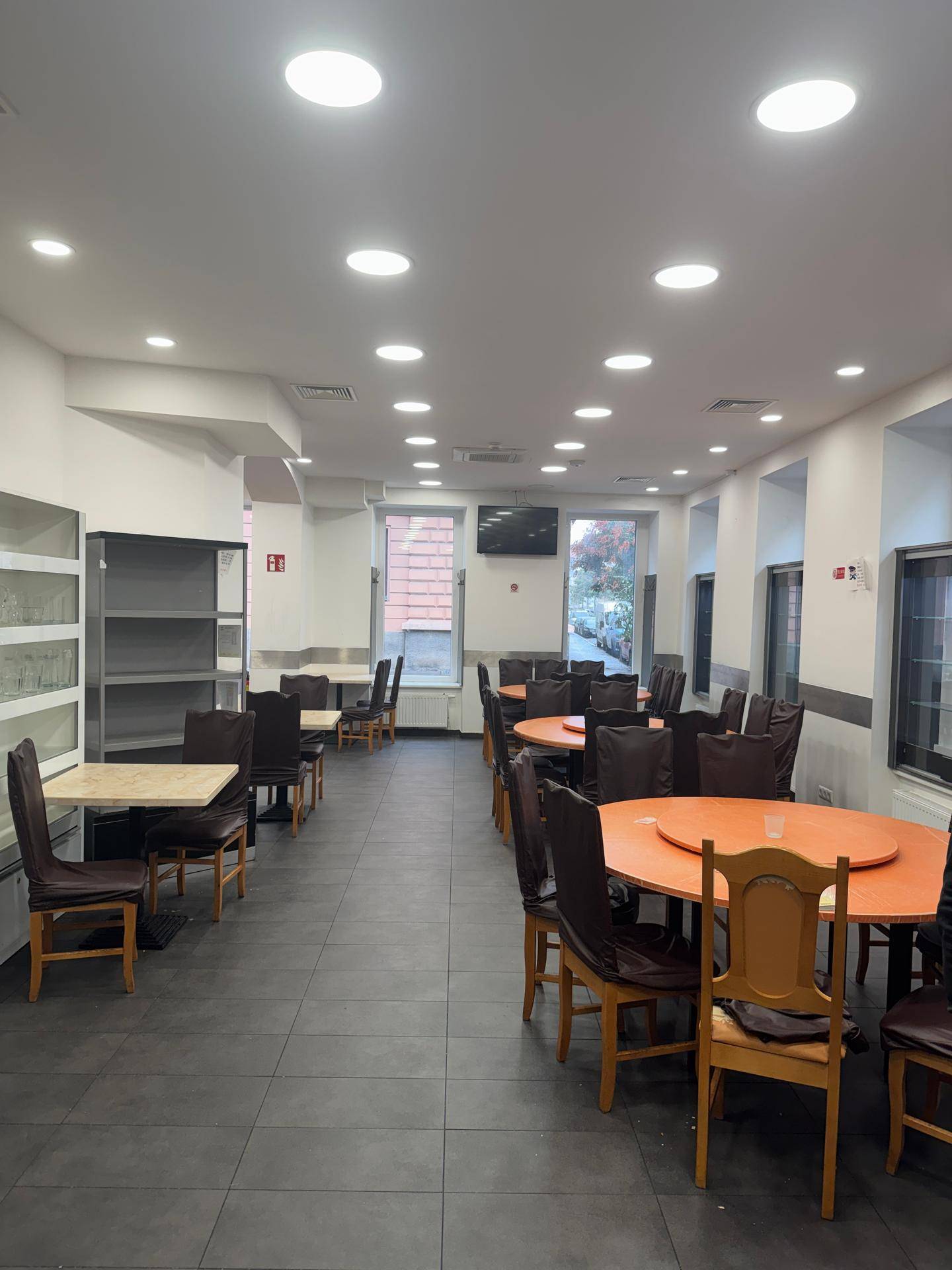 Heller Restaurantraum mit mehreren Tischen, Stühlen und Regalen an der Wand.