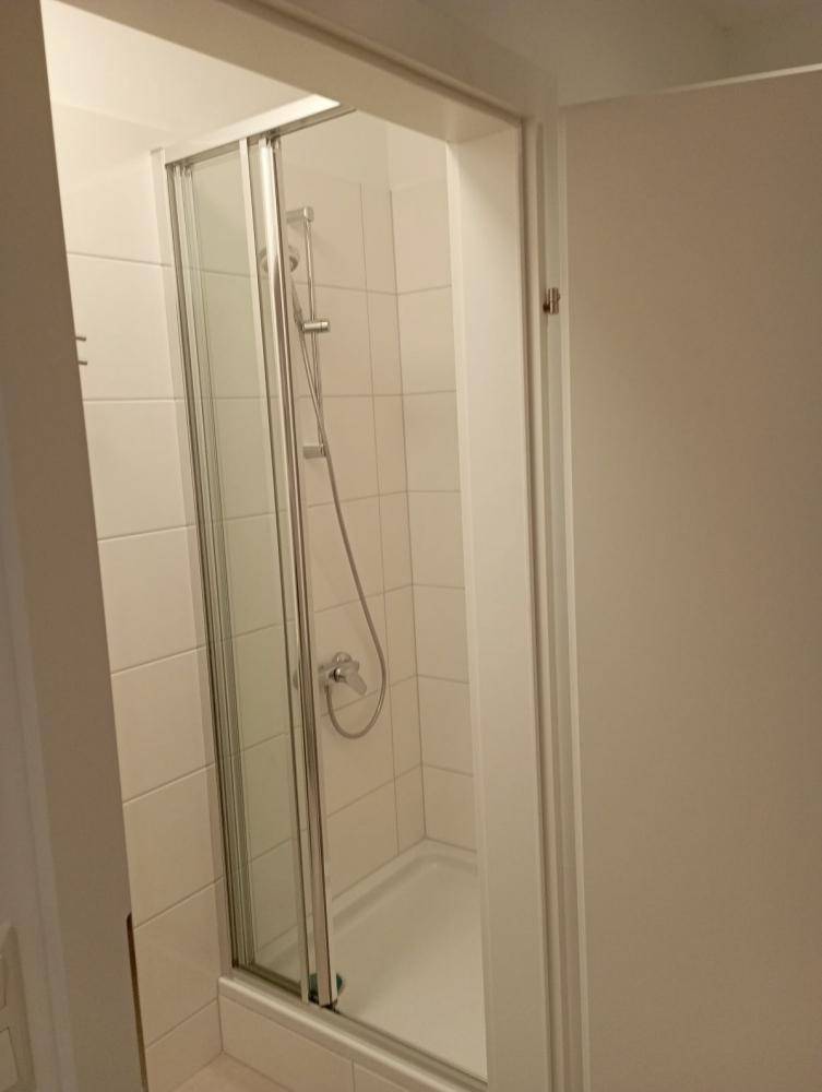 Duschbereich in einem Badezimmer mit Glasfalttür und weißen Wandfliesen.