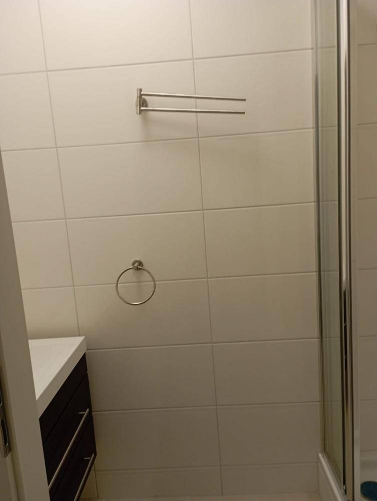 Badezimmer mit Duschkabine, weißen Fliesen und Handtuchhaltern an der Wand.