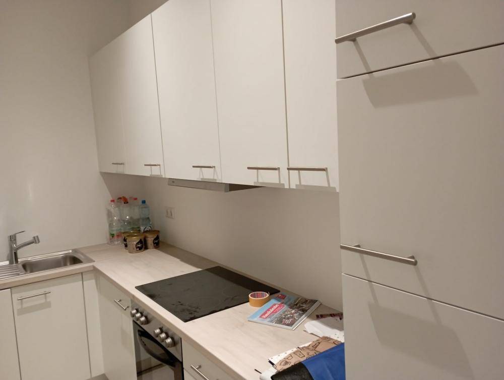 Helle Küche mit weißen Hängeschränken, Kochfeld und Arbeitsplatte.