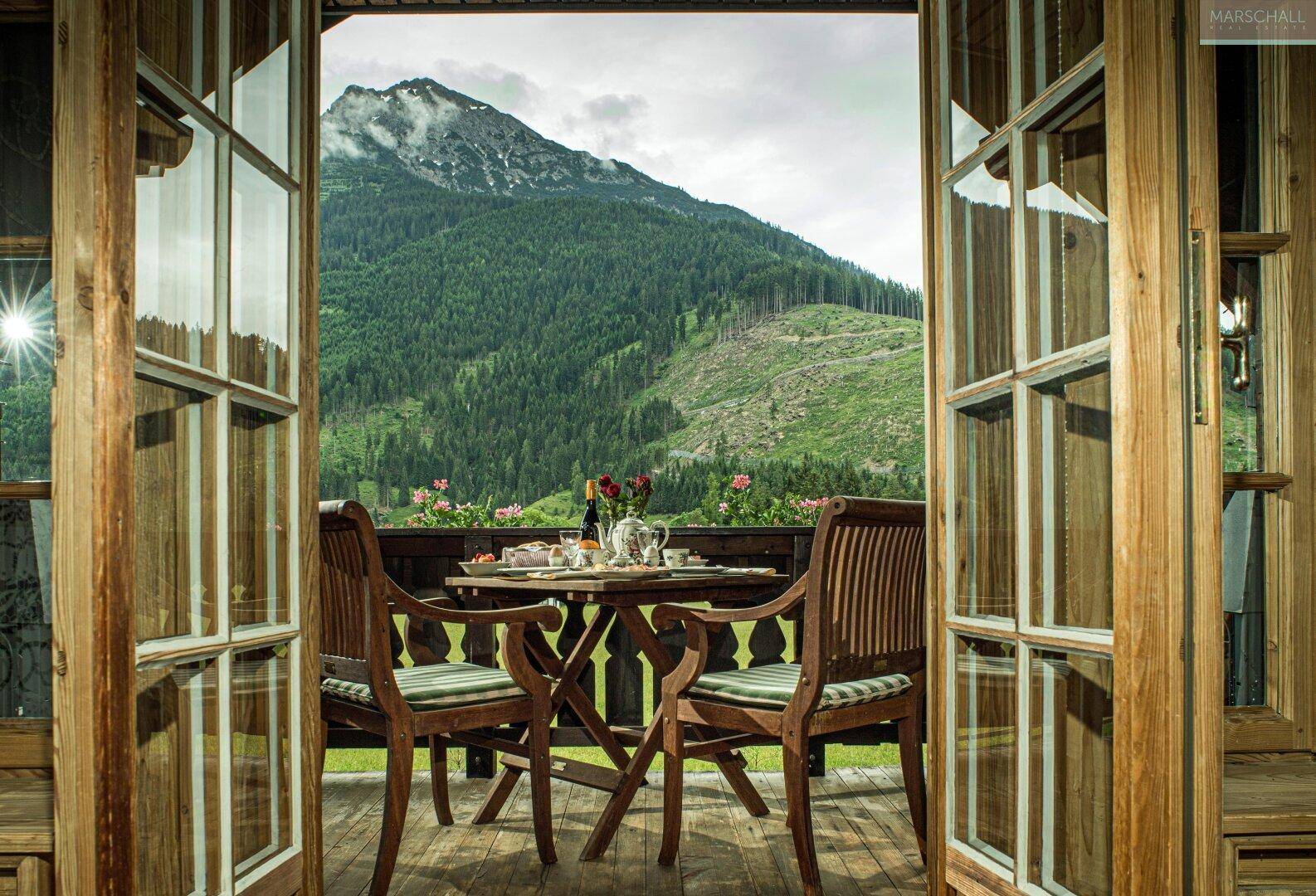Balkon mit Holztisch und Stühlen, bietet einen atemberaubenden Blick auf die umliegenden Berge.