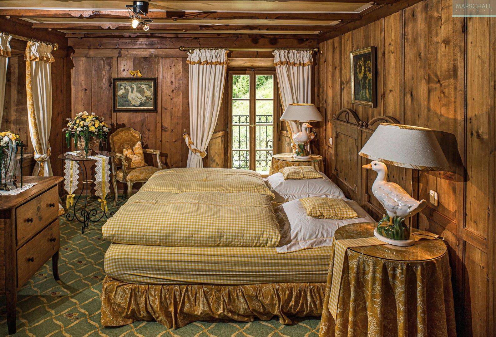 Gemütliches Schlafzimmer mit Holzvertäfelung, traditionellen Möbeln und Zugang zu einem französischen Balkon.