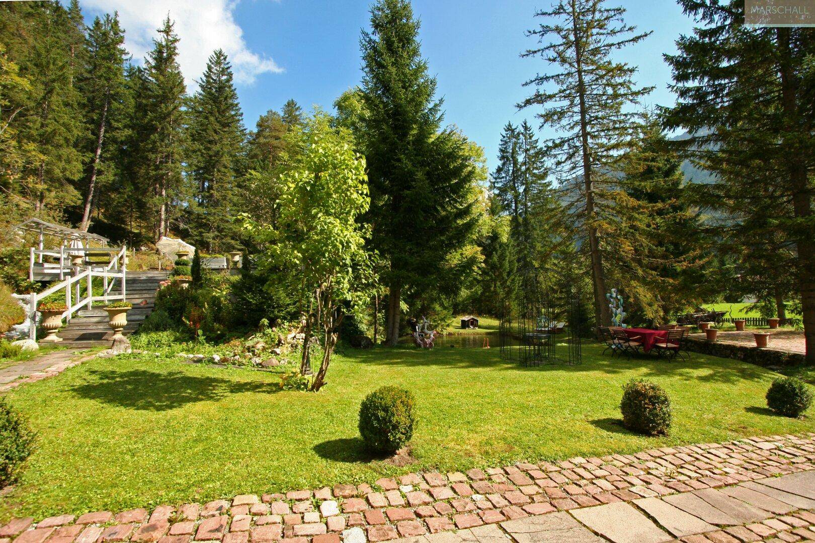 Weitläufiger, gepflegter Garten mit Rasenflächen, Bäumen und einem Ziegelweg, ideal zum Entspannen.