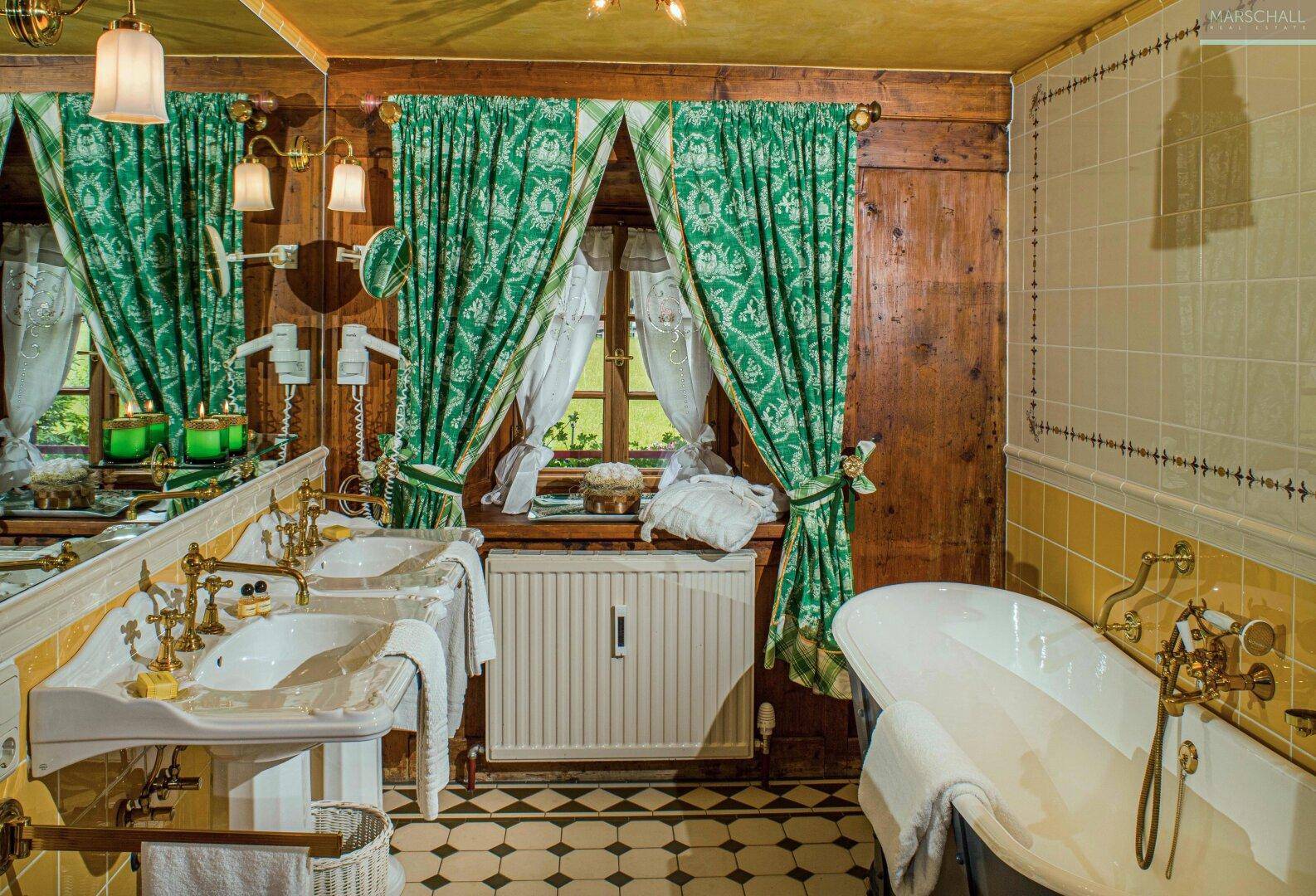 Traditionelles Badezimmer mit zwei Waschbecken, freistehender Badewanne und grünen Vorhängen.