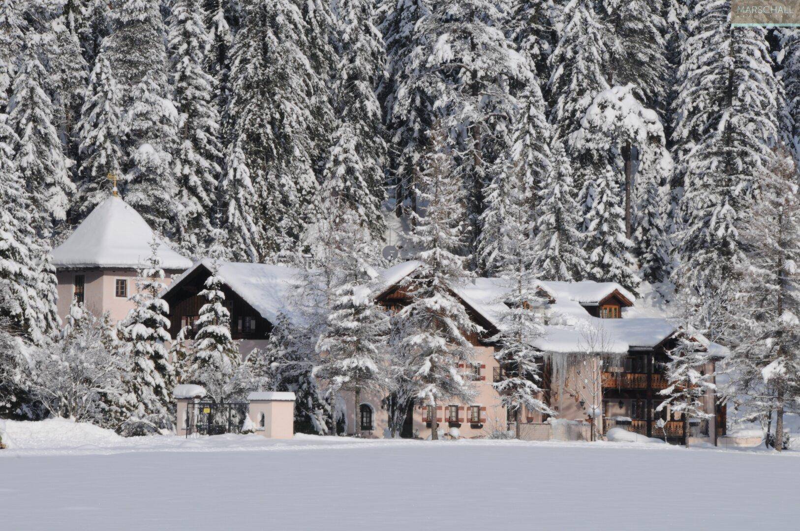 Weitläufiges Anwesen im Winter, umgeben von tief verschneiten Wäldern und Bergen.
