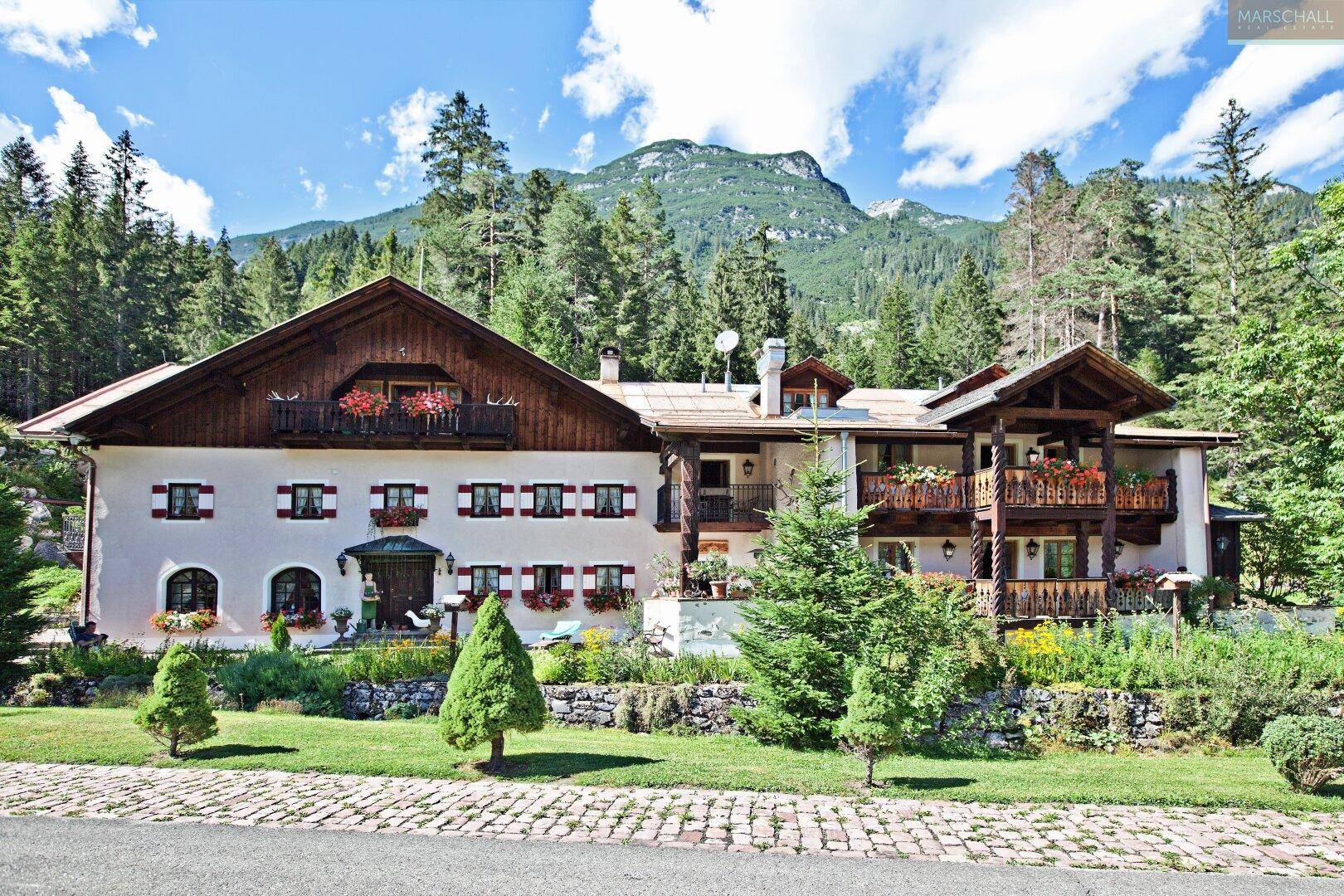 Traditionelles Alpenhaus mit Balkonen und Blumenkästen, umgeben von einem gepflegten Garten und Bergen.
