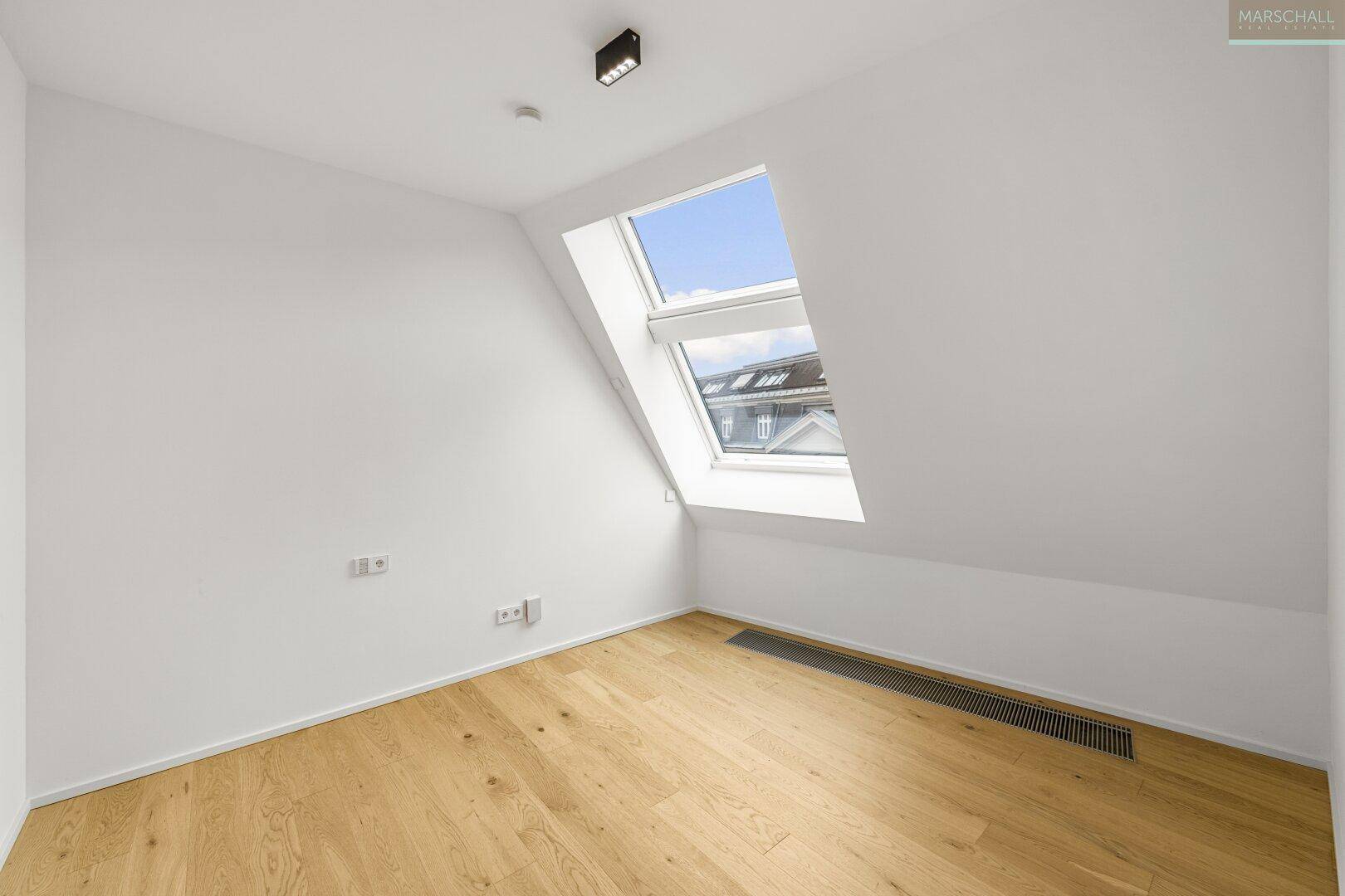Leeres Zimmer mit Holzboden und einem Dachfenster, ideal als Schlaf- oder Arbeitszimmer.