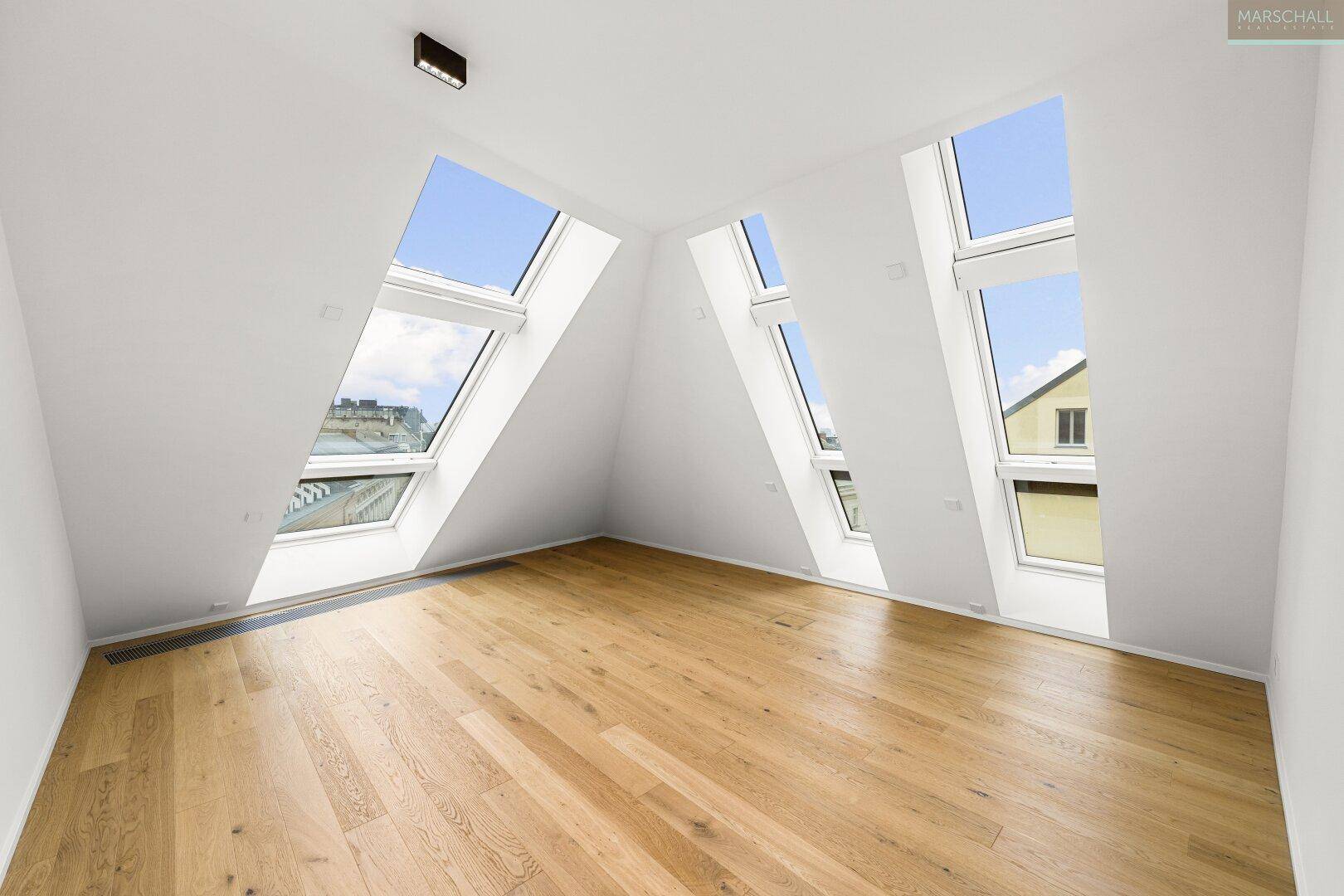 Helles Zimmer mit Holzboden und großen Dachfenstern, die viel Licht hereinlassen.