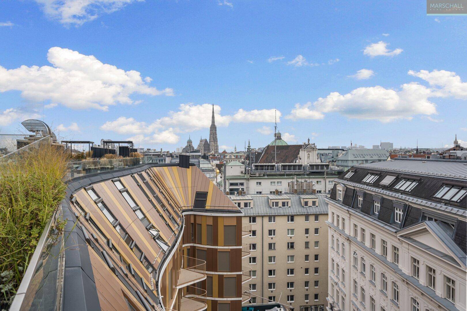 Panoramablick über die Dächer Wiens mit dem Stephansdom im Hintergrund unter blauem Himmel.