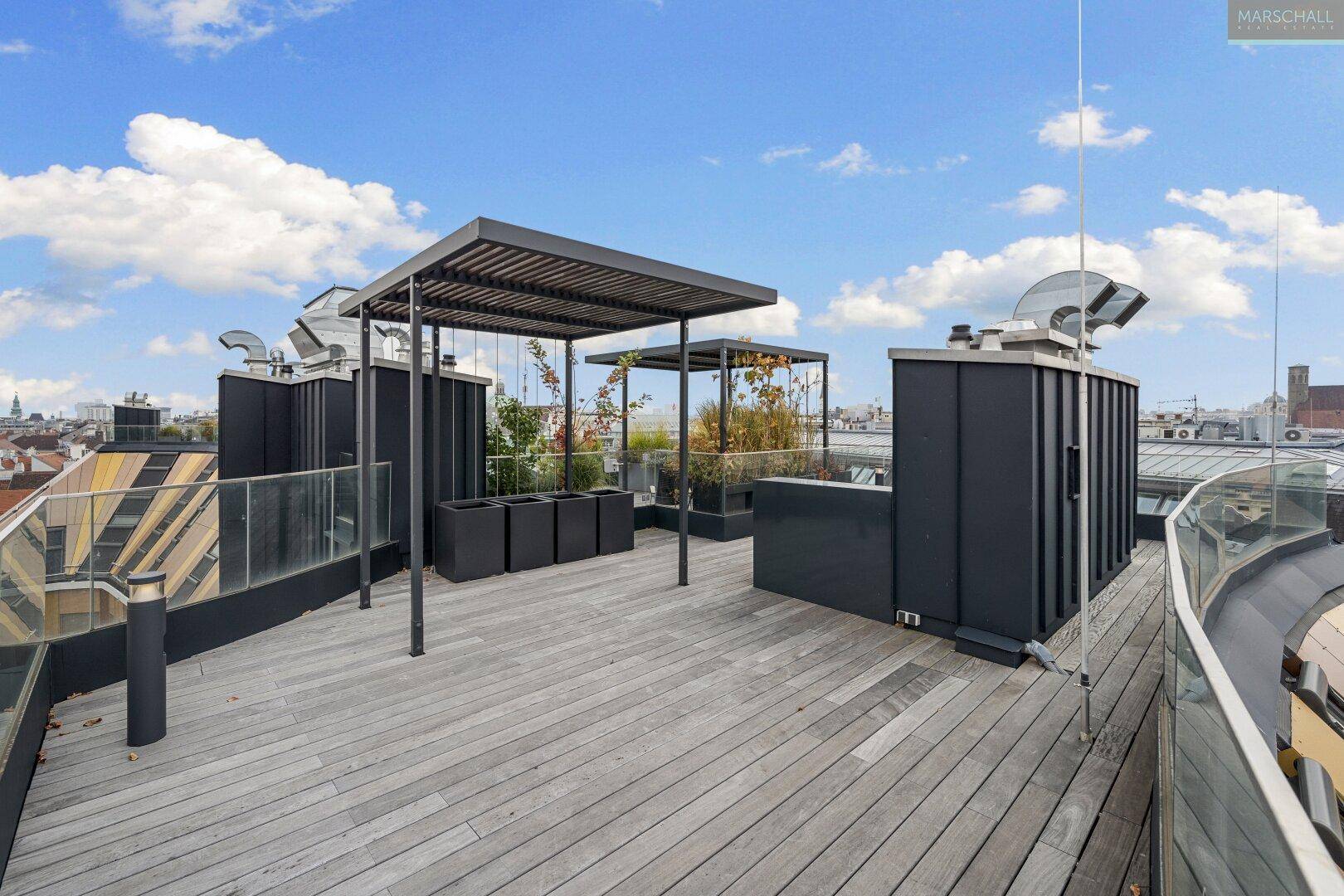 Geräumige Dachterrasse mit Holzbelag, Pergola und Blick auf die Stadt.