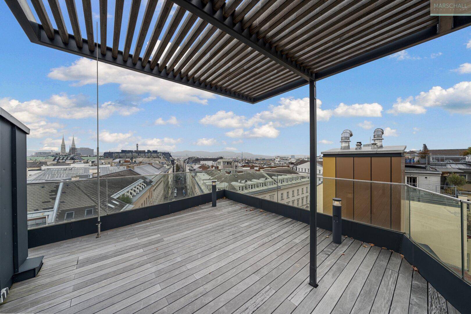 Weitläufige Dachterrasse mit Holzdeck, Pergola und Panoramablick über die Wiener Skyline.