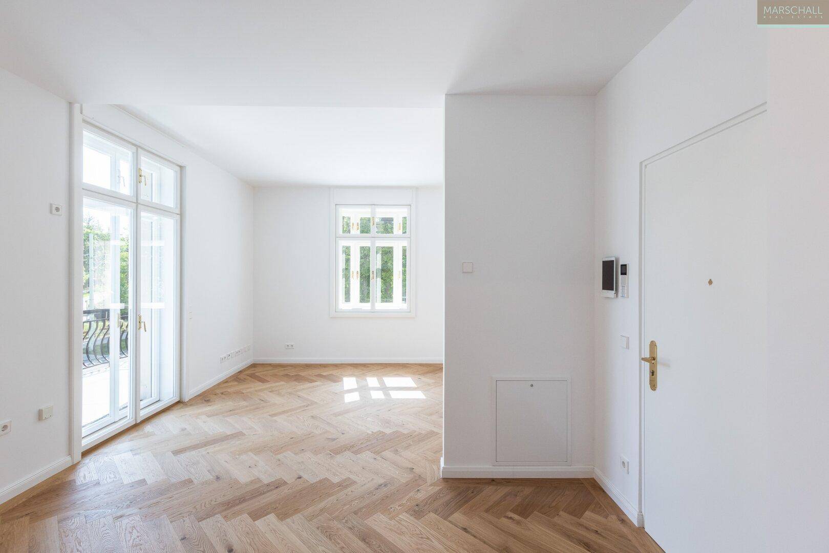 Heller Eingangsbereich mit Fischgrätparkett und Zugang zu weiteren Räumen sowie einem Balkon.