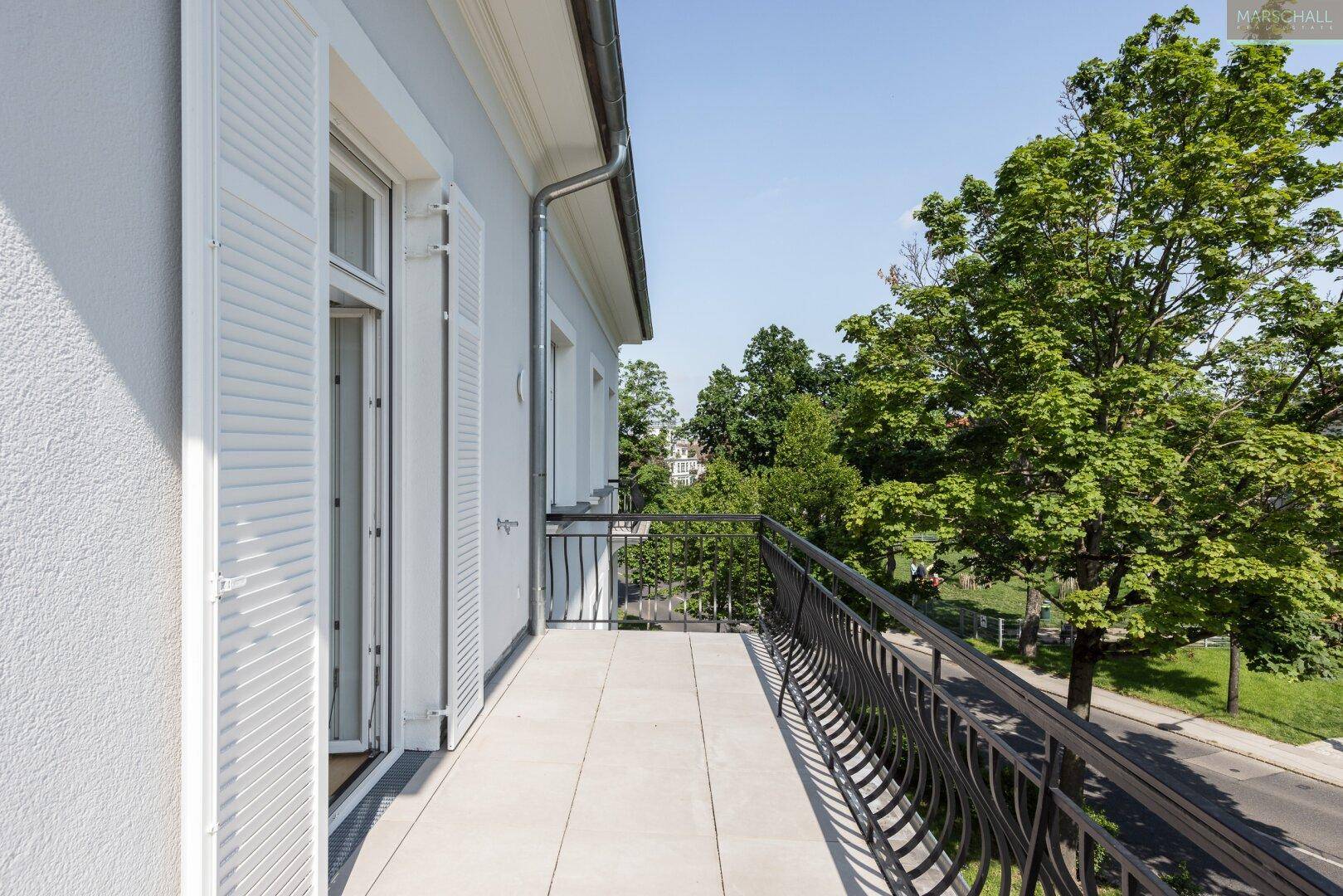 Geräumiger Balkon mit schmiedeeisernem Geländer und Blick auf Bäume und die Straße.