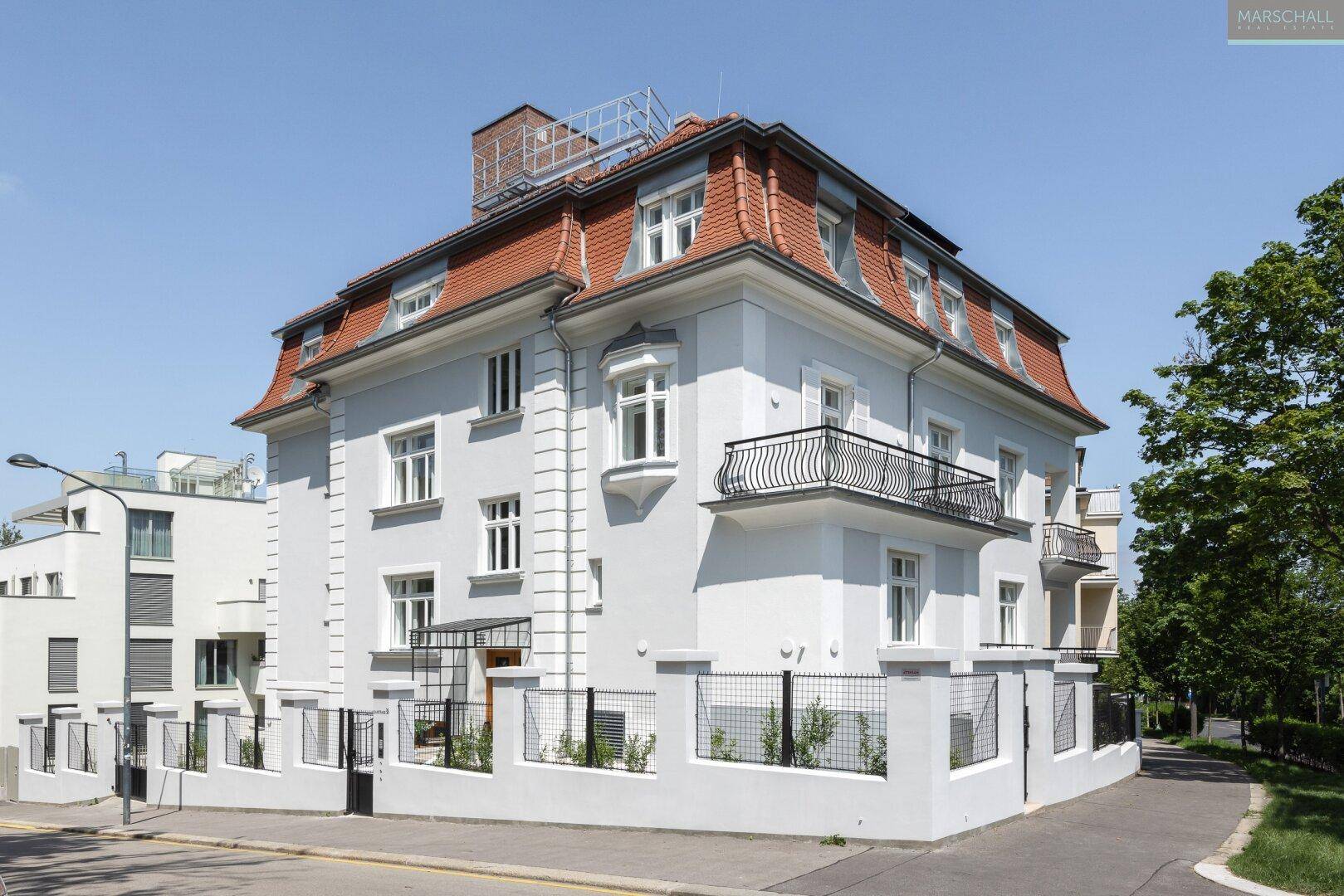 Elegantes Altbaugebäude mit klassischer Architektur, hellblauer Fassade und roten Mansarddächern.
