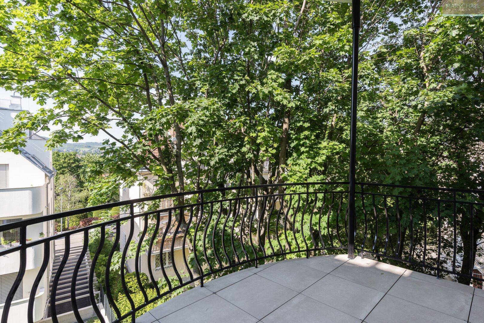 Geräumiger Balkon mit schmiedeeisernem Geländer und üppigem Grünblick.