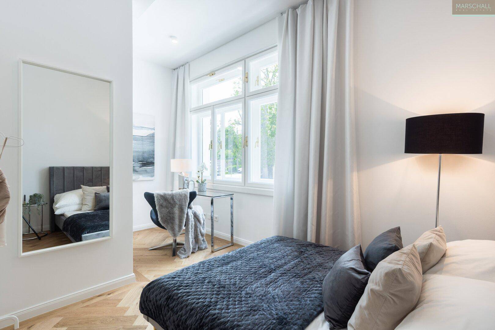 Gemütliches Schlafzimmer mit Parkettboden, großen Fenstern und einem modernen Spiegel als Dekoration.