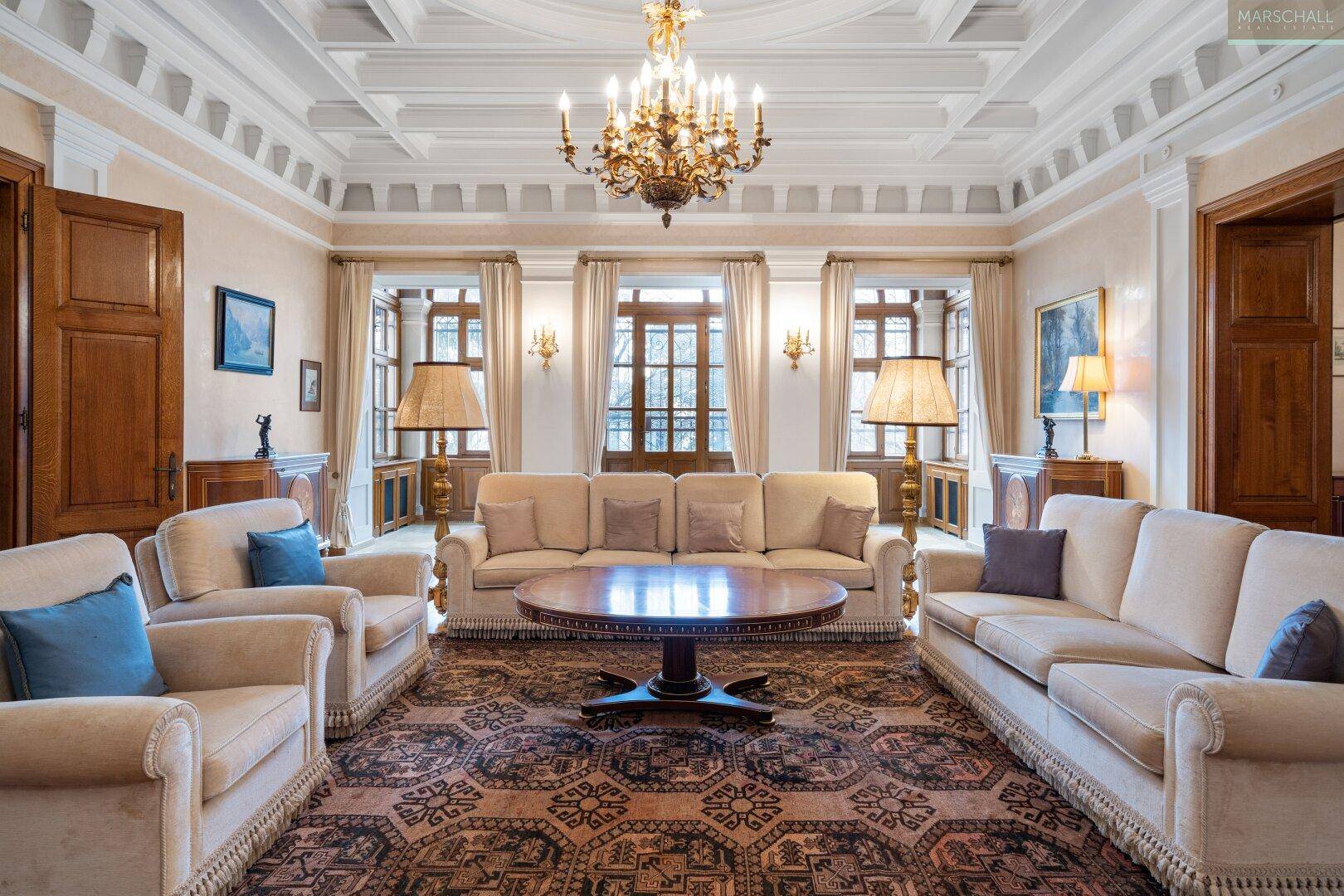 Elegantes Wohnzimmer mit Stuckdecke, Kronleuchter und bequemen Sofas in hellem Ambiente.