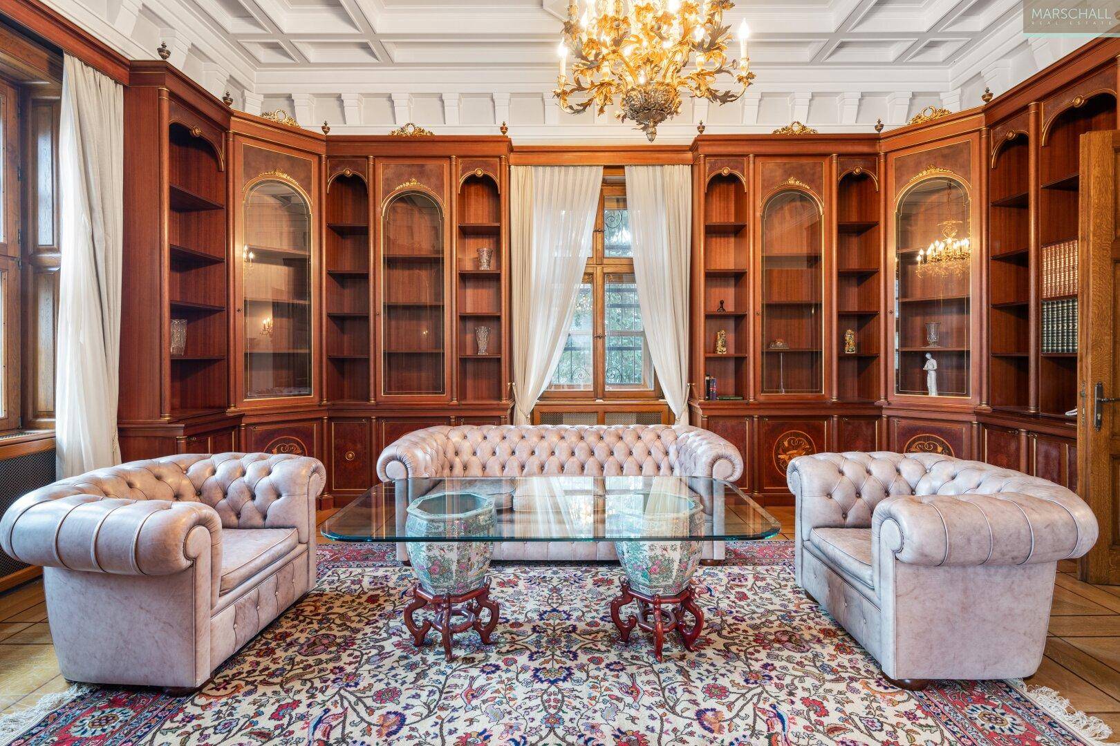 Exklusive Bibliothek mit maßgefertigten Holzregalen, Chesterfield-Möbeln und opulentem Kronleuchter.
