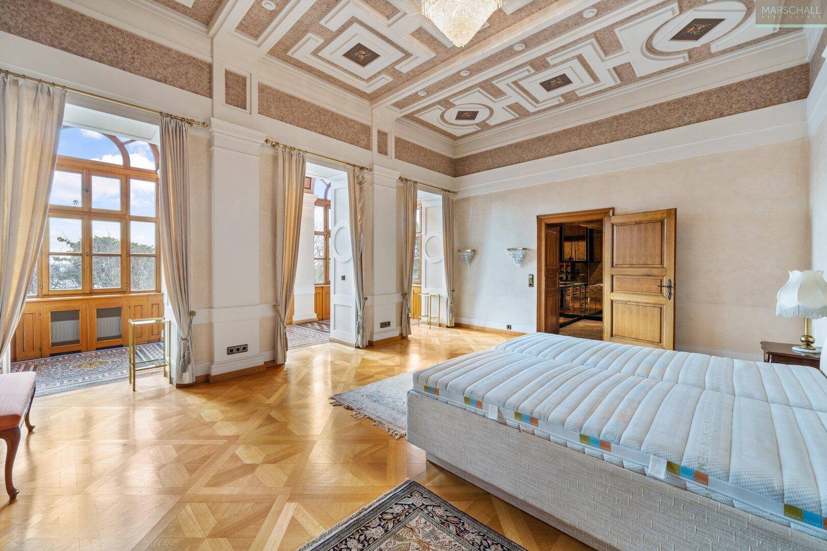 Geräumiges Schlafzimmer mit Parkettboden, hohen Decken und Zugang zu einem Wintergarten oder Balkon.