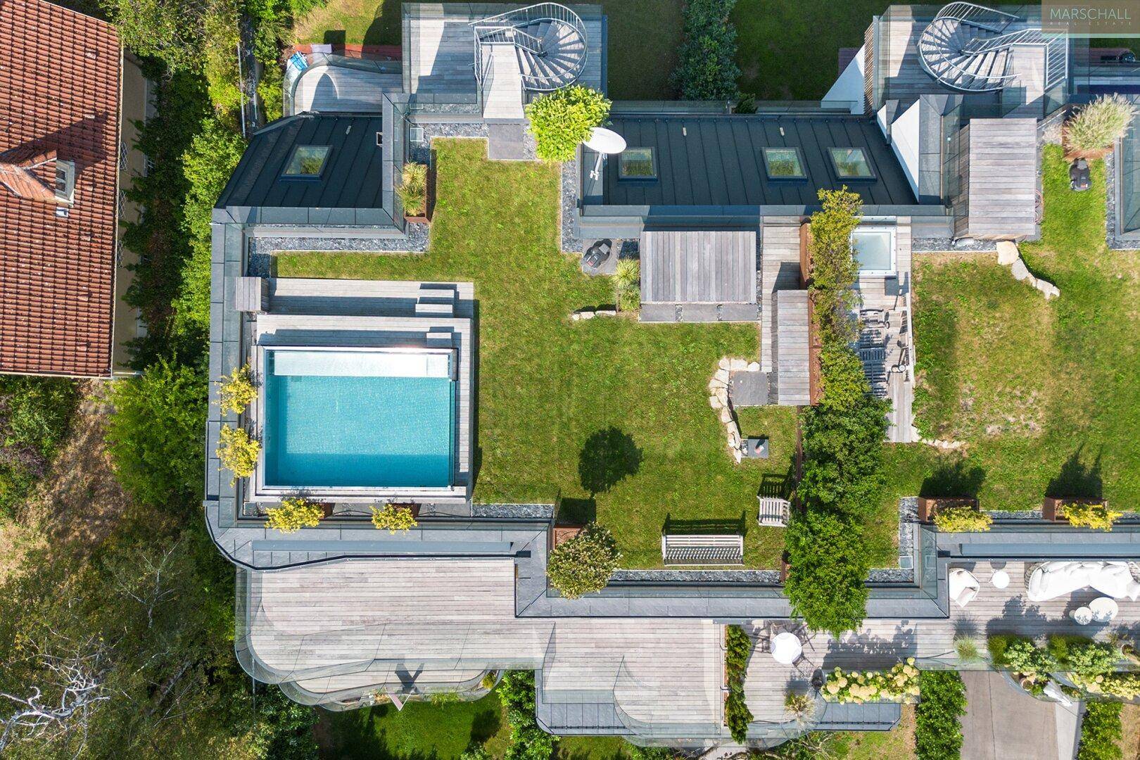 Luftaufnahme eines modernen Gebäudekomplexes mit mehreren Pools, Dachgärten und Terrassenbereichen.