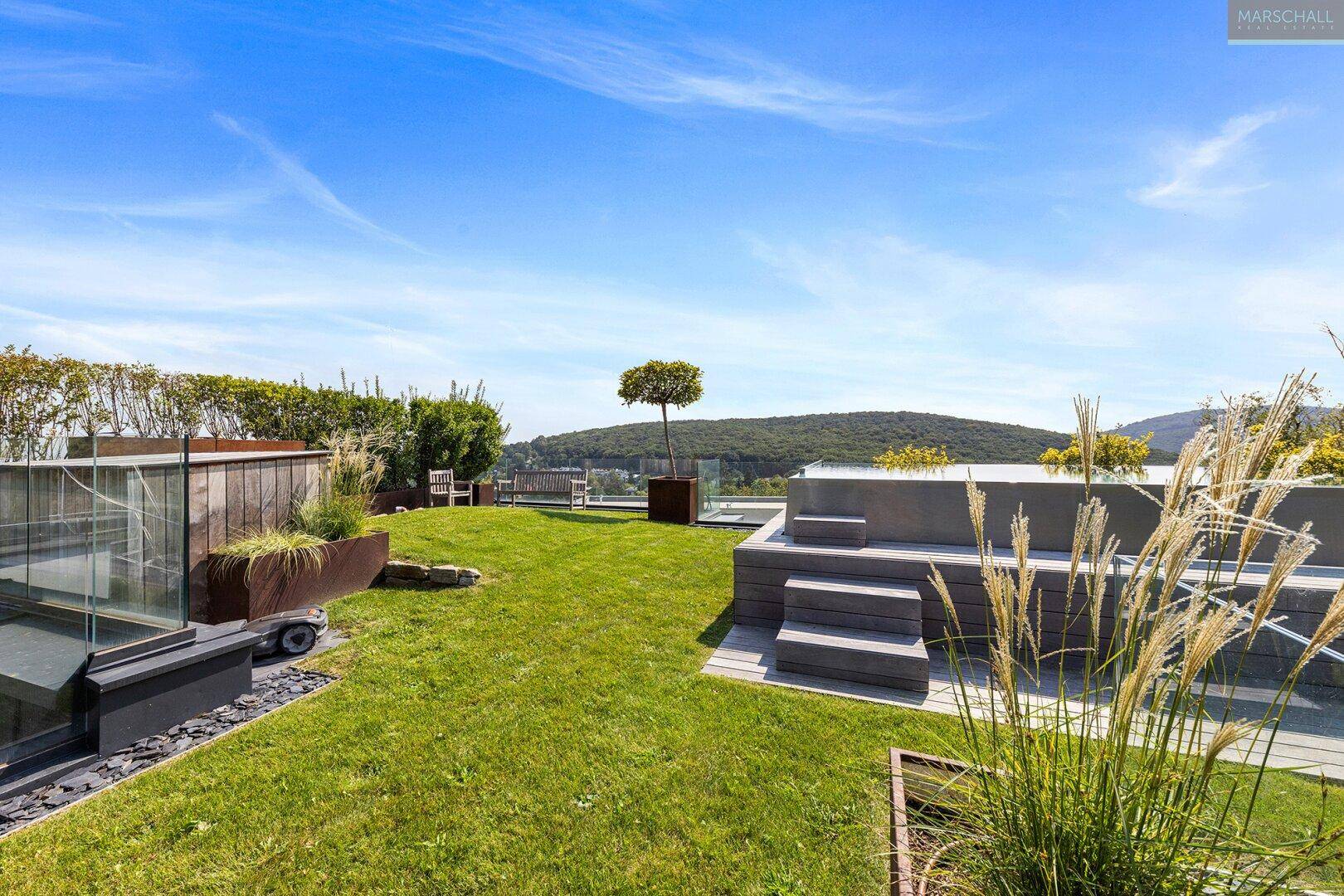 Grüne Dachterrasse mit Rasenfläche, Pflanzenkübeln und Sitzgelegenheiten unter klarem Himmel.