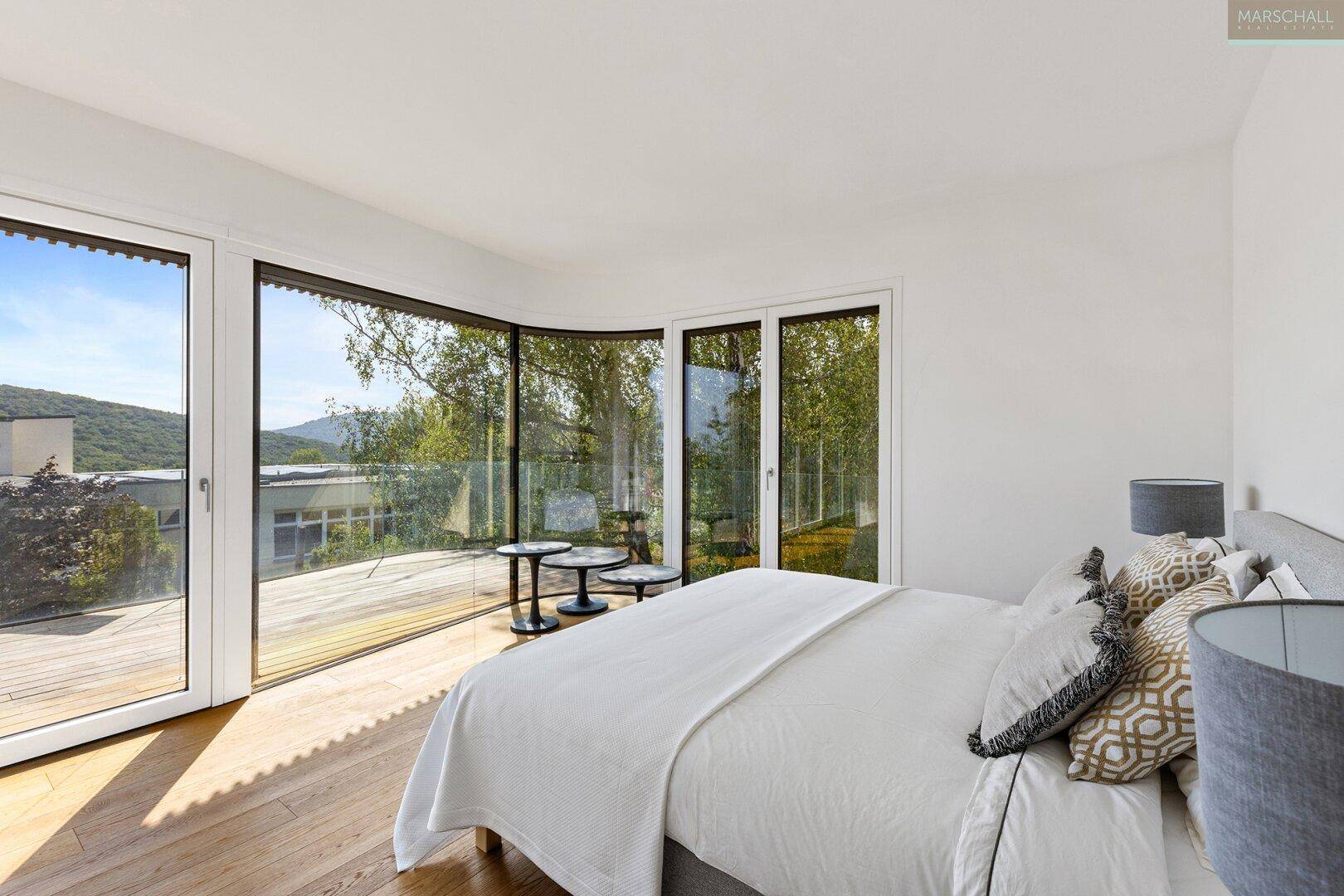 Helles Schlafzimmer mit Holzboden, großen Fenstern und direktem Zugang zu einer Außenterrasse.