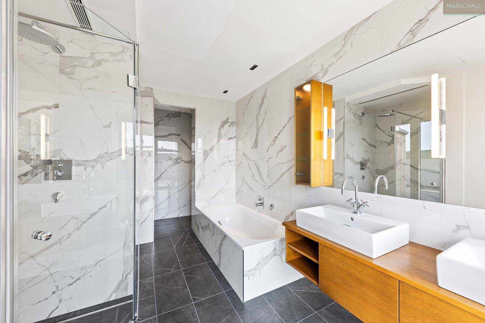Modernes Badezimmer mit Marmorfliesen, großer Badewanne, Duschkabine und Doppelwaschbecken.