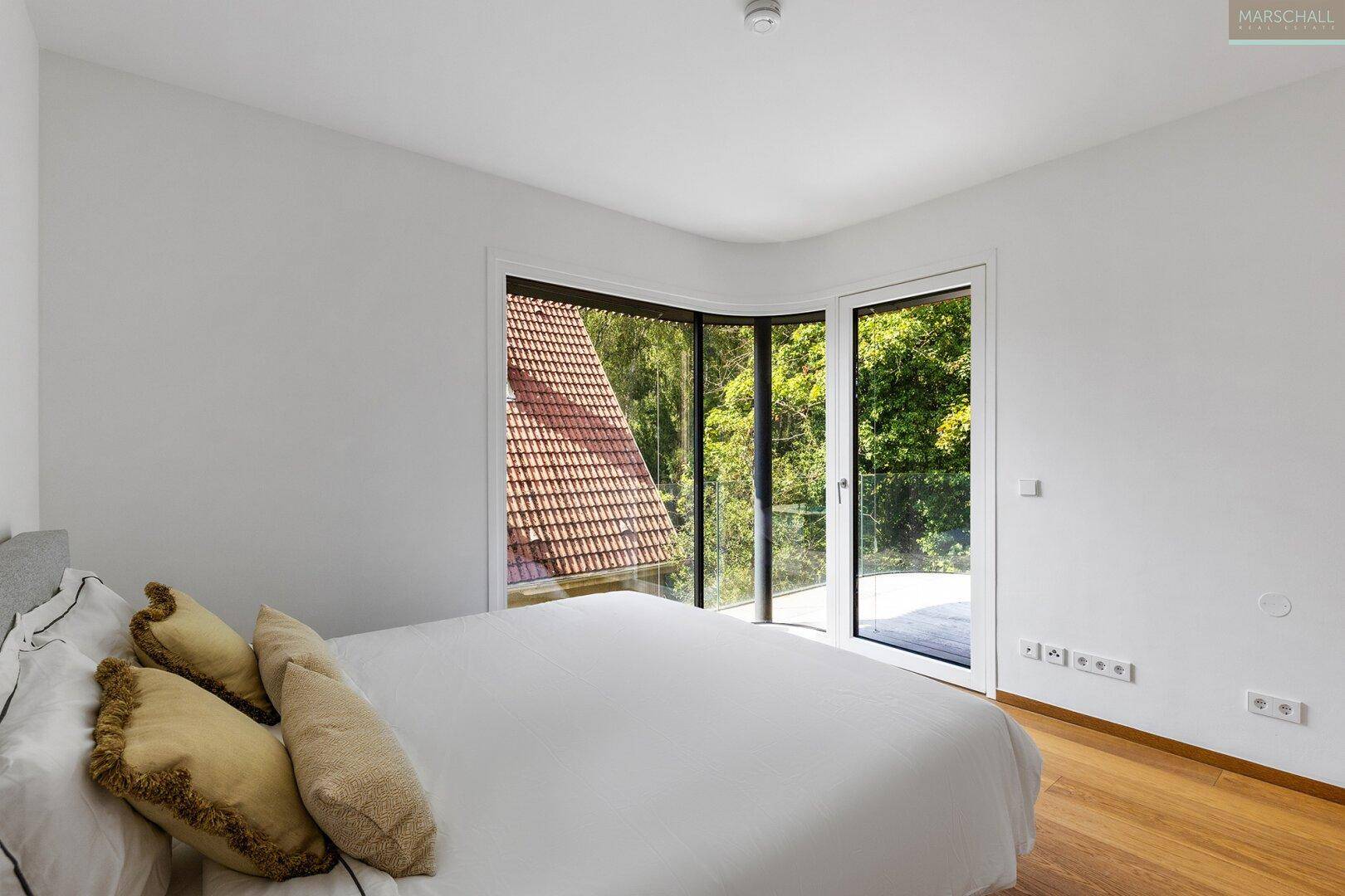 Schlafzimmer mit Holzboden und großen Fenstern, die einen Blick auf die umliegende Natur bieten.