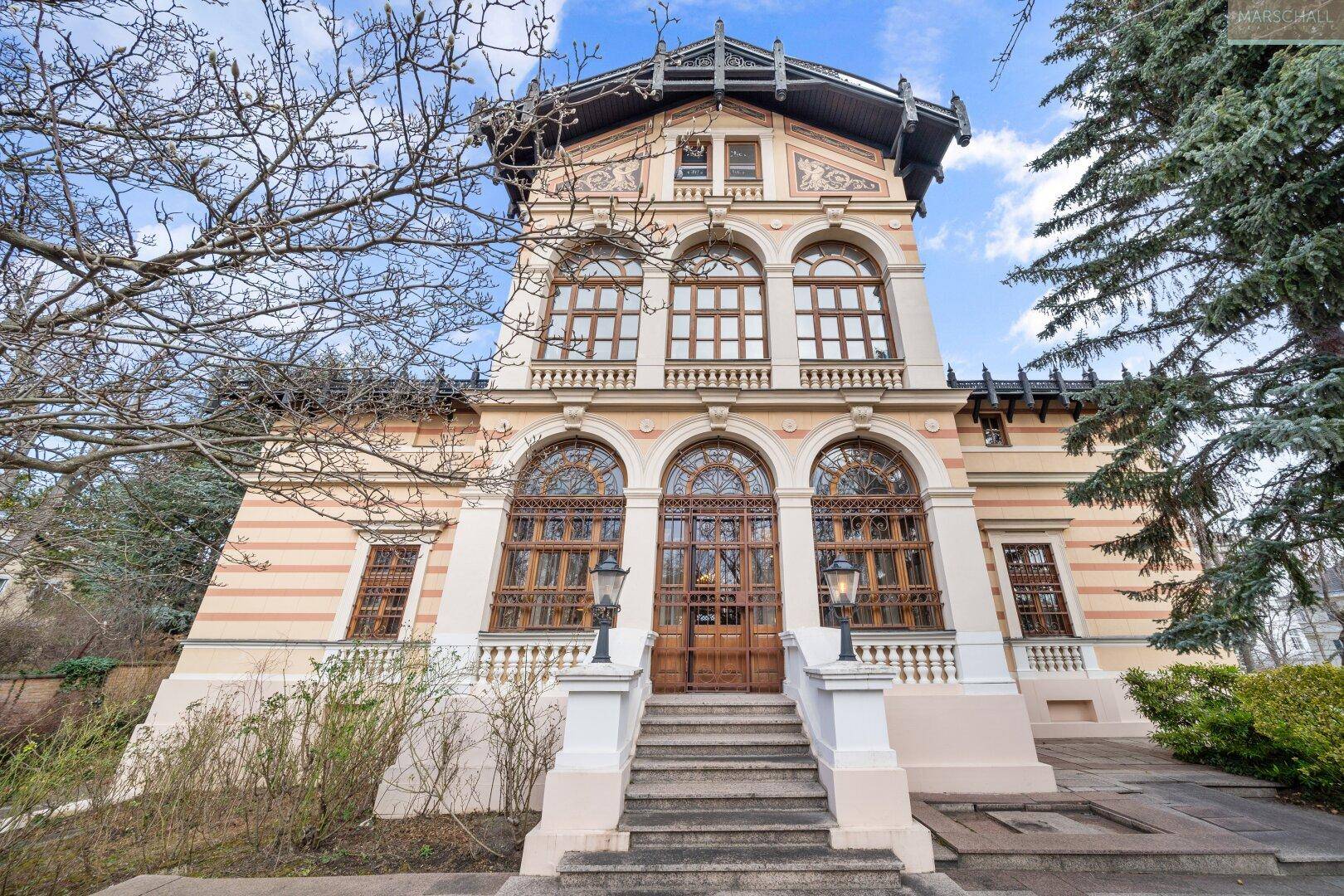 Prächtige Fassade einer historischen Villa mit großen Bogenfenstern und imposantem Eingangsbereich.