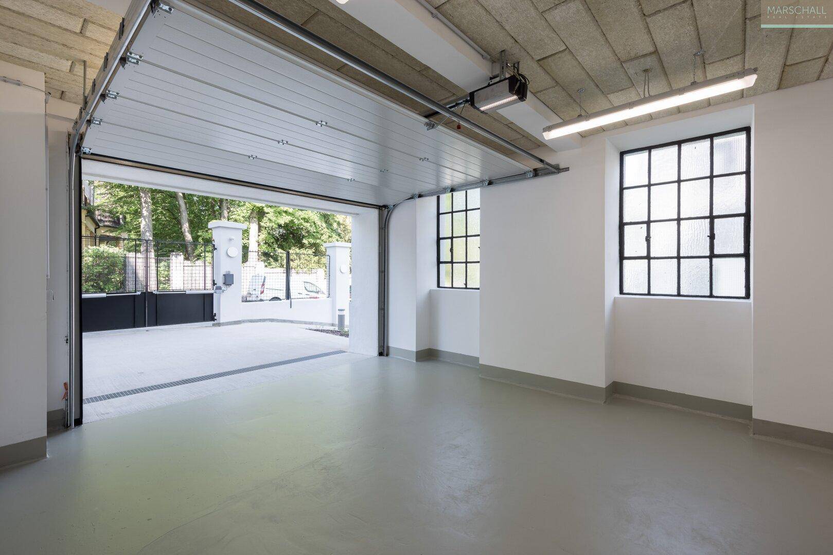 Geräumige Garage mit automatischem Tor, Fenstern und ausreichend Platz für Fahrzeuge.